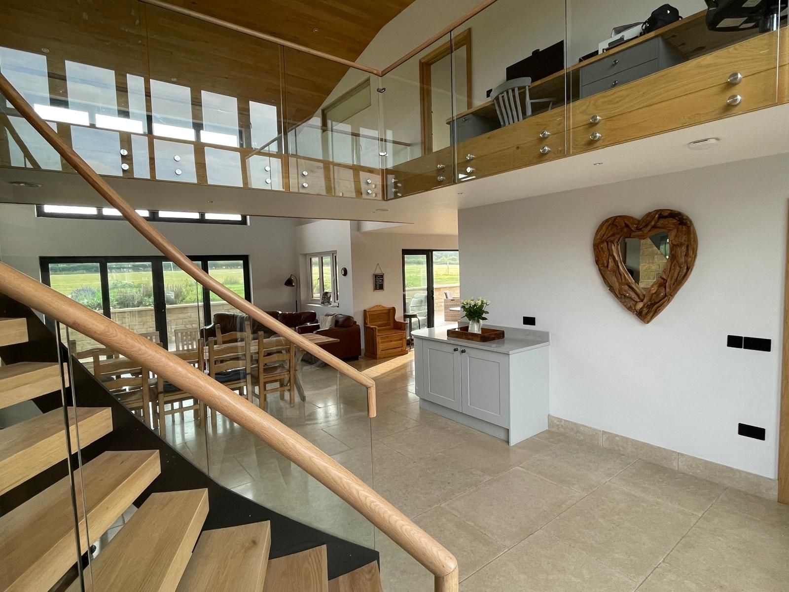 Modern, open-plan living space with a wooden staircase, glass balcony, and a heart-shaped mirror on a white wall.
