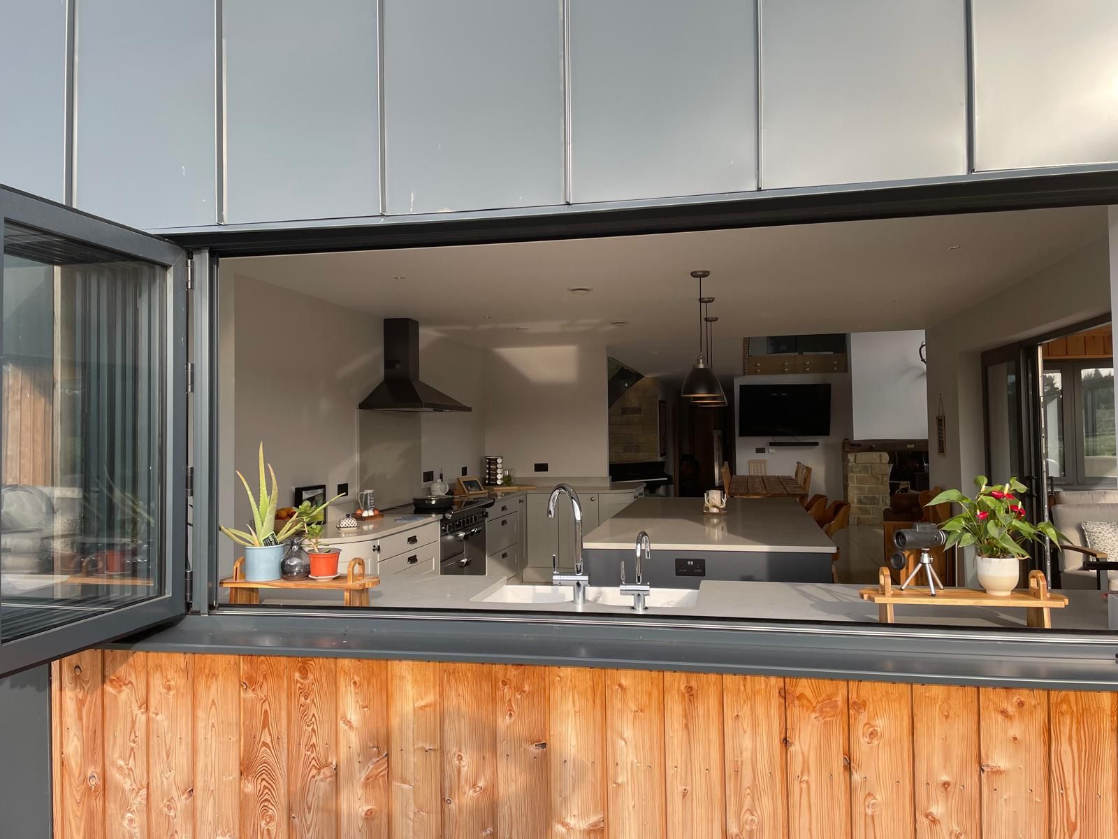 A bright, modern kitchen interior viewed through a large open pass-through window with wooden paneling on the exterior.