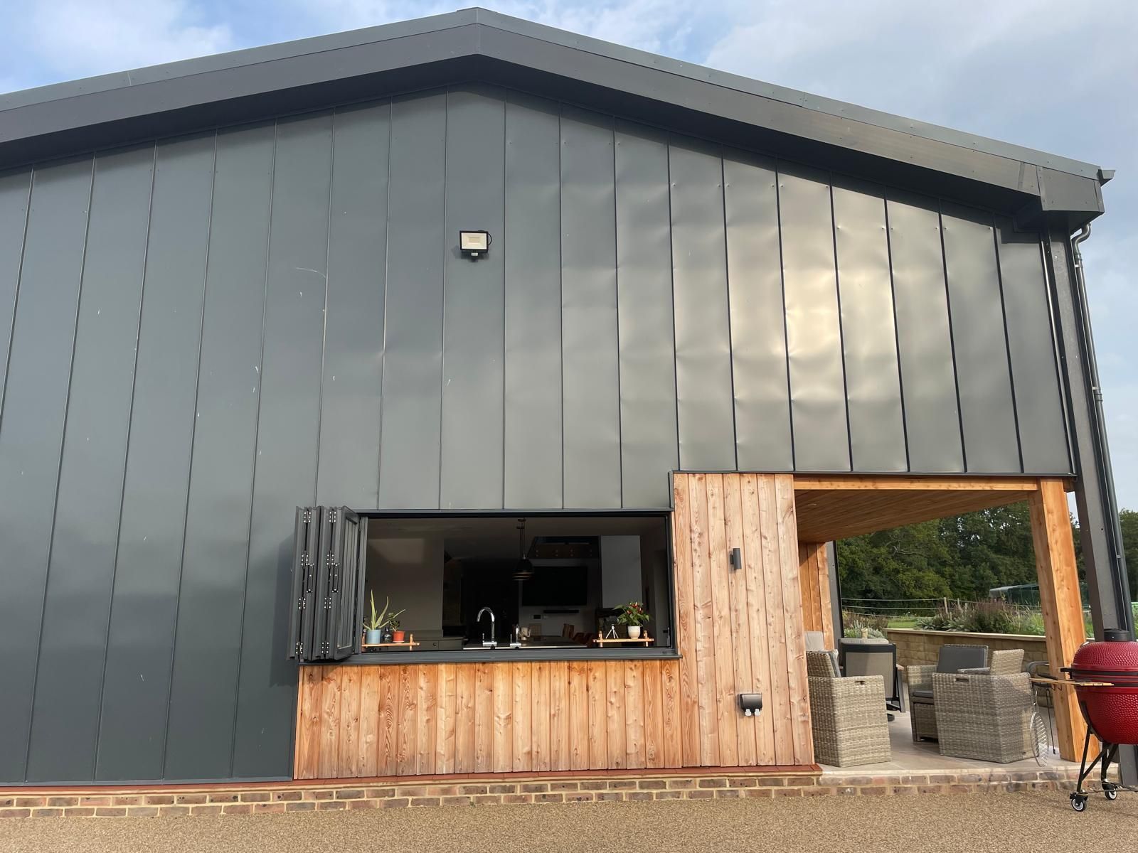 Modern building exterior with dark grey standing-seam metal siding, a wood-paneled serving bar, and an open patio area.