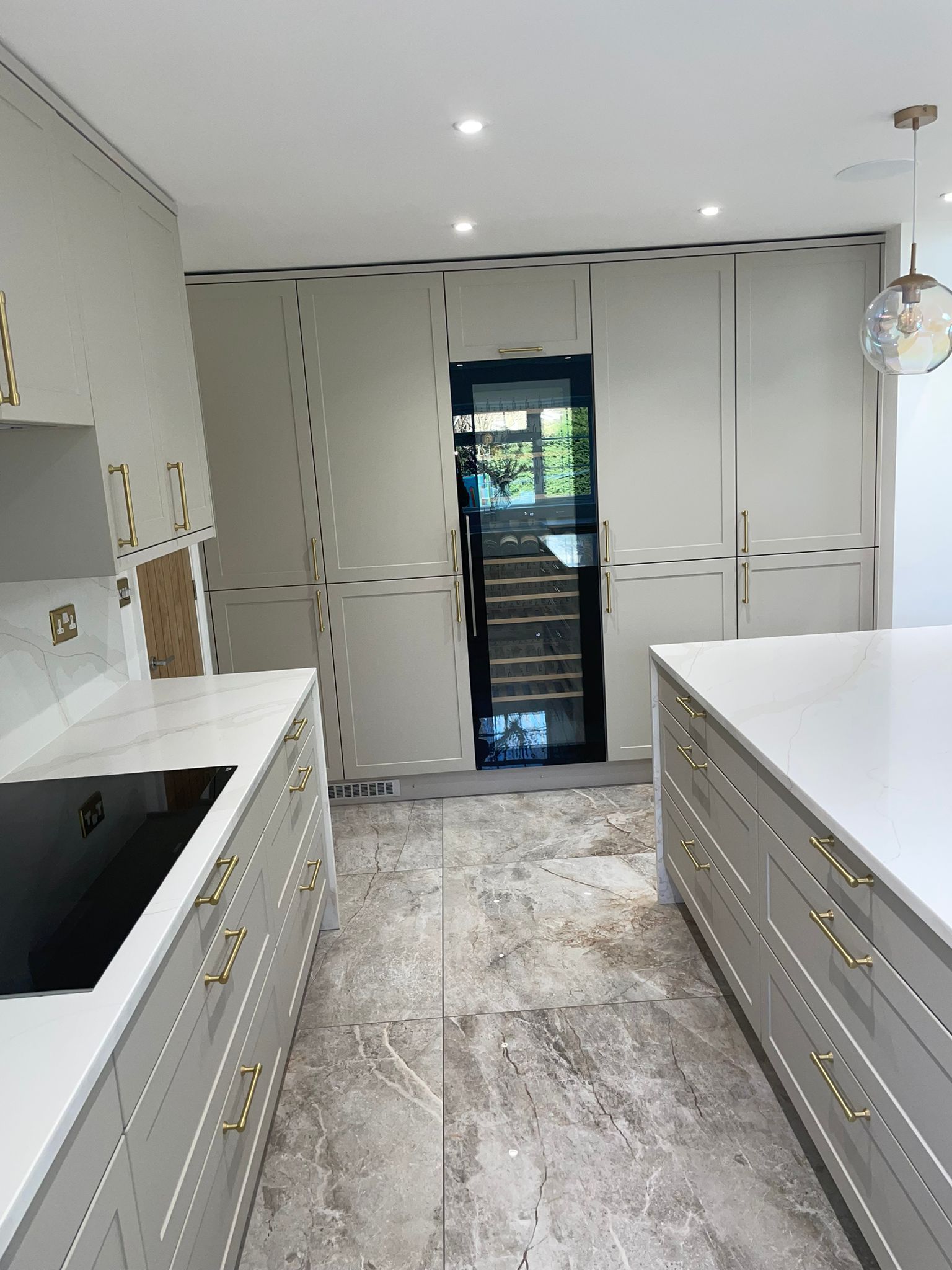 A modern kitchen with grey cabinetry, gold hardware, white countertops, and marble-patterned flooring.