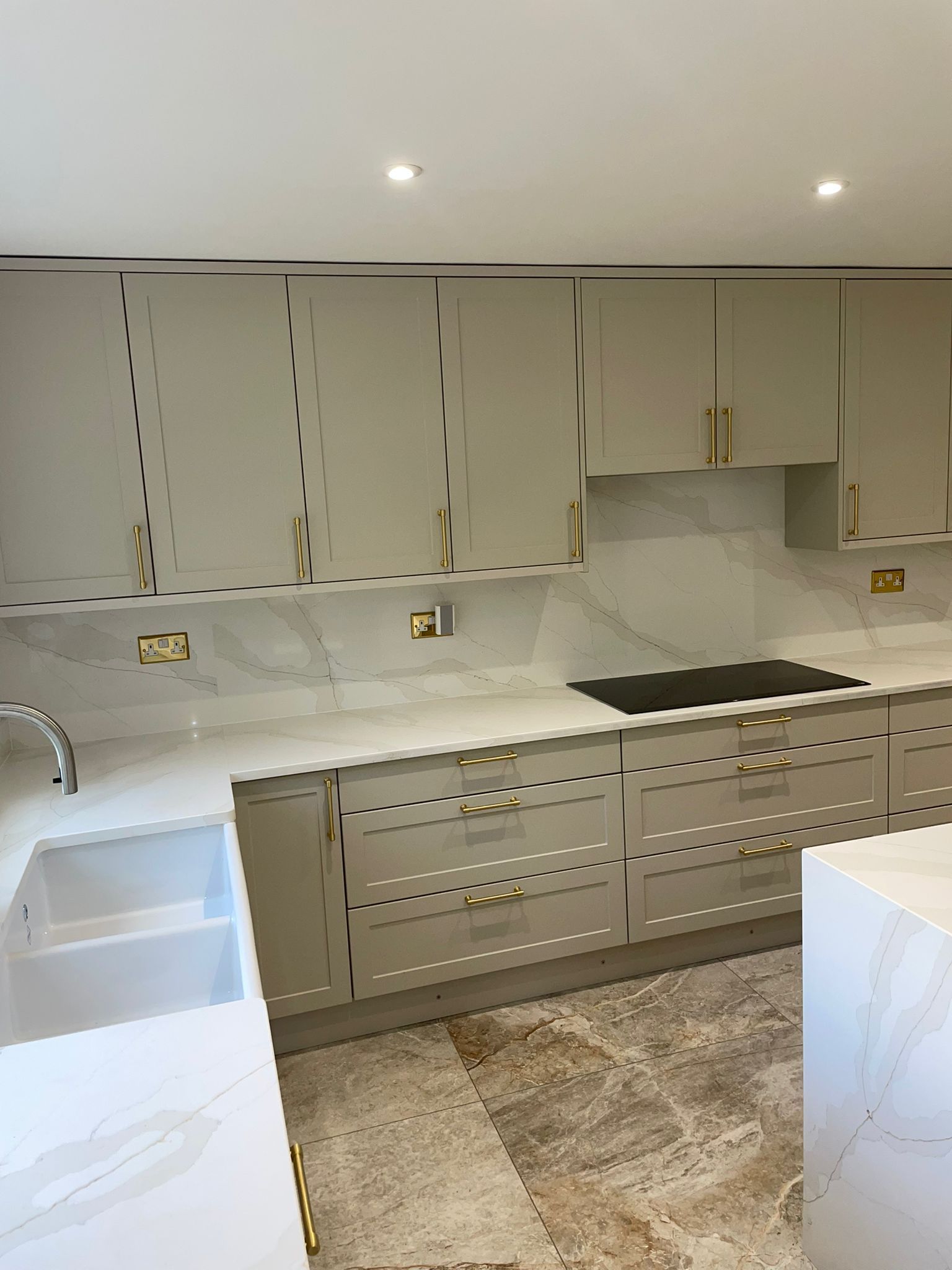 A modern kitchen with light gray cabinetry, gold hardware, marble countertops, and tiled floors.