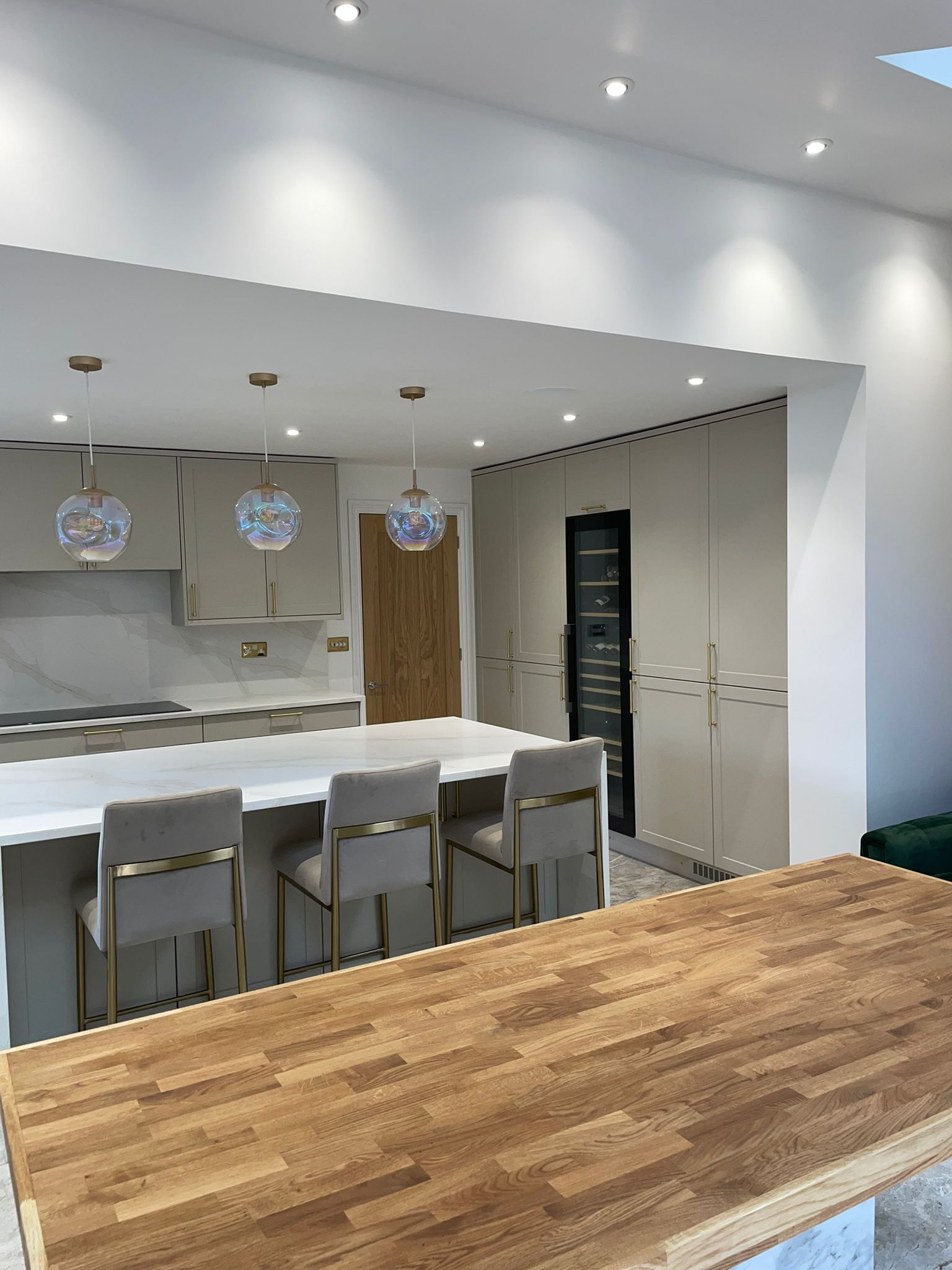 A modern, open-plan kitchen with a white marble island, light grey bar stools, pendant lighting, and tall beige cabinets.