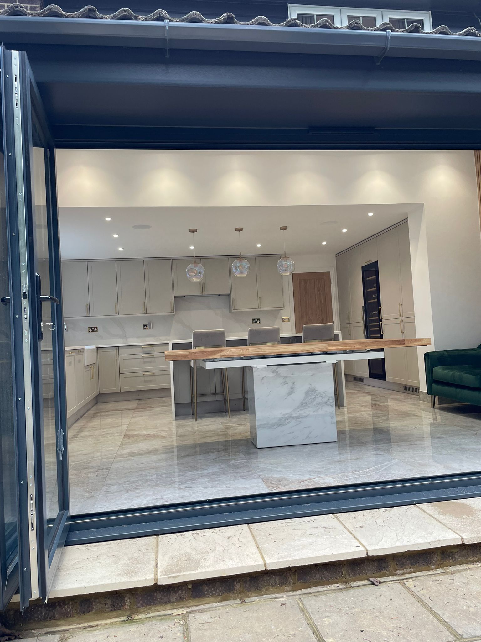A modern open-plan kitchen seen through bi-fold doors, featuring a white marble island with a live-edge wooden countertop.