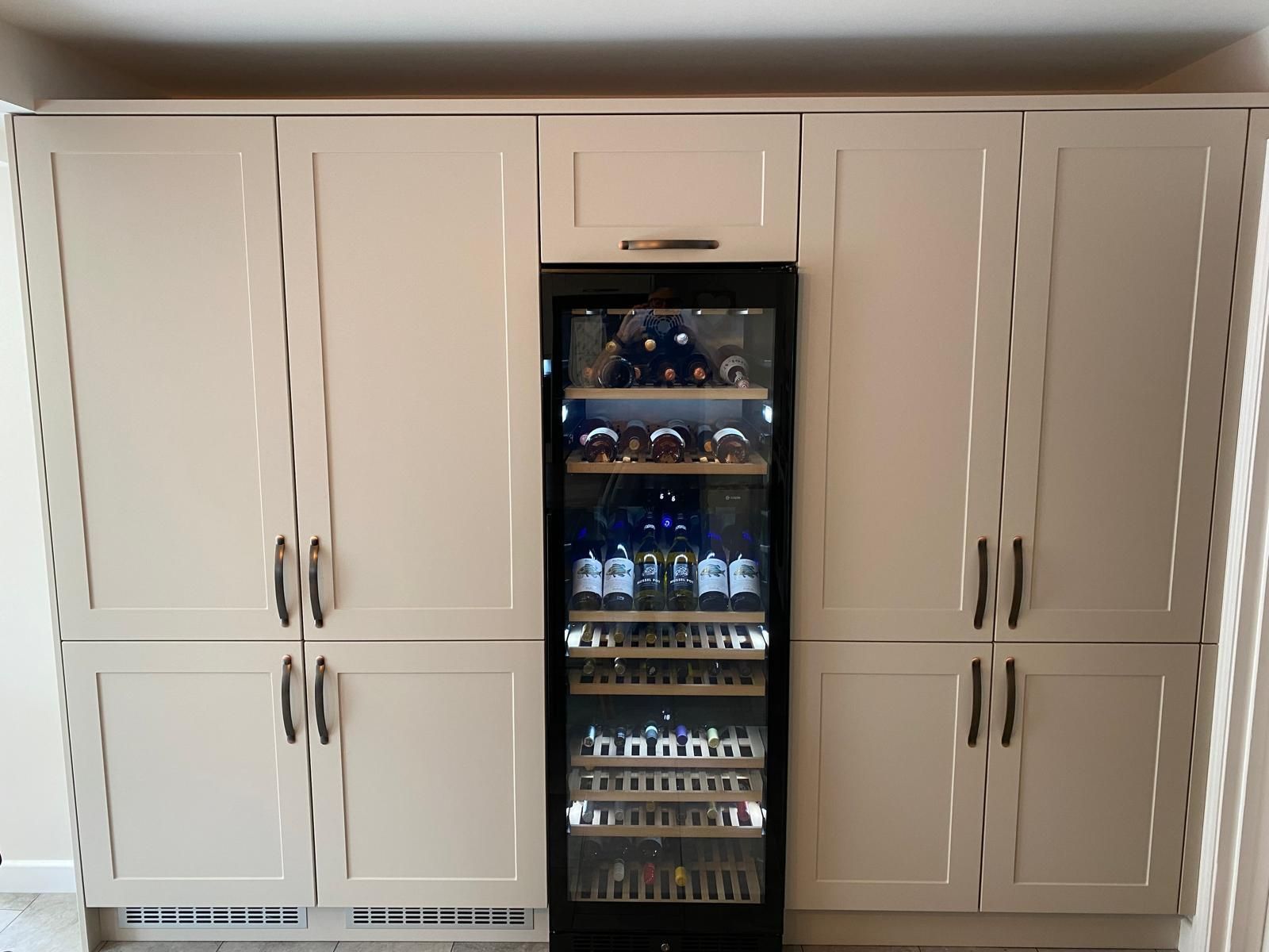 A tall, cream-colored cabinet unit with two double-door cupboards flanking a central, built-in glass wine refrigerator.