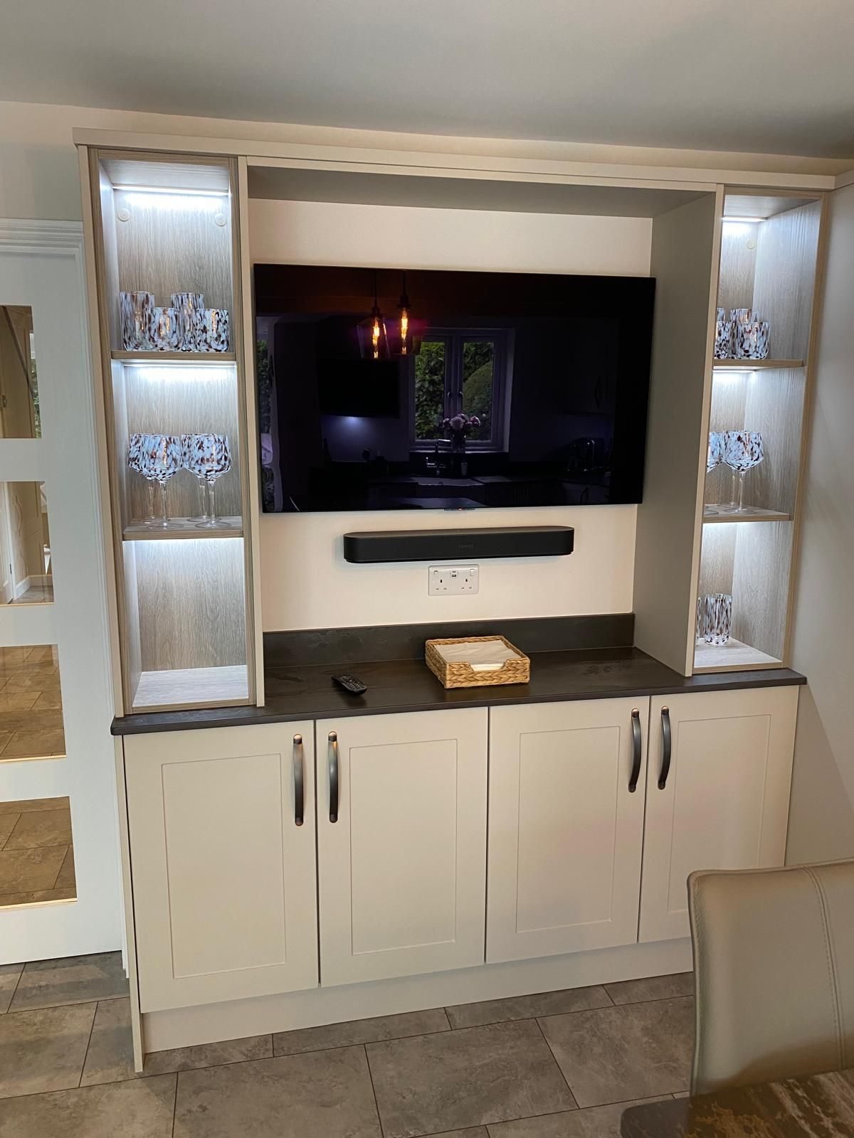 Cream-colored built-in cabinets and shelves featuring an integrated television, soundbar, and illuminated glass shelves.