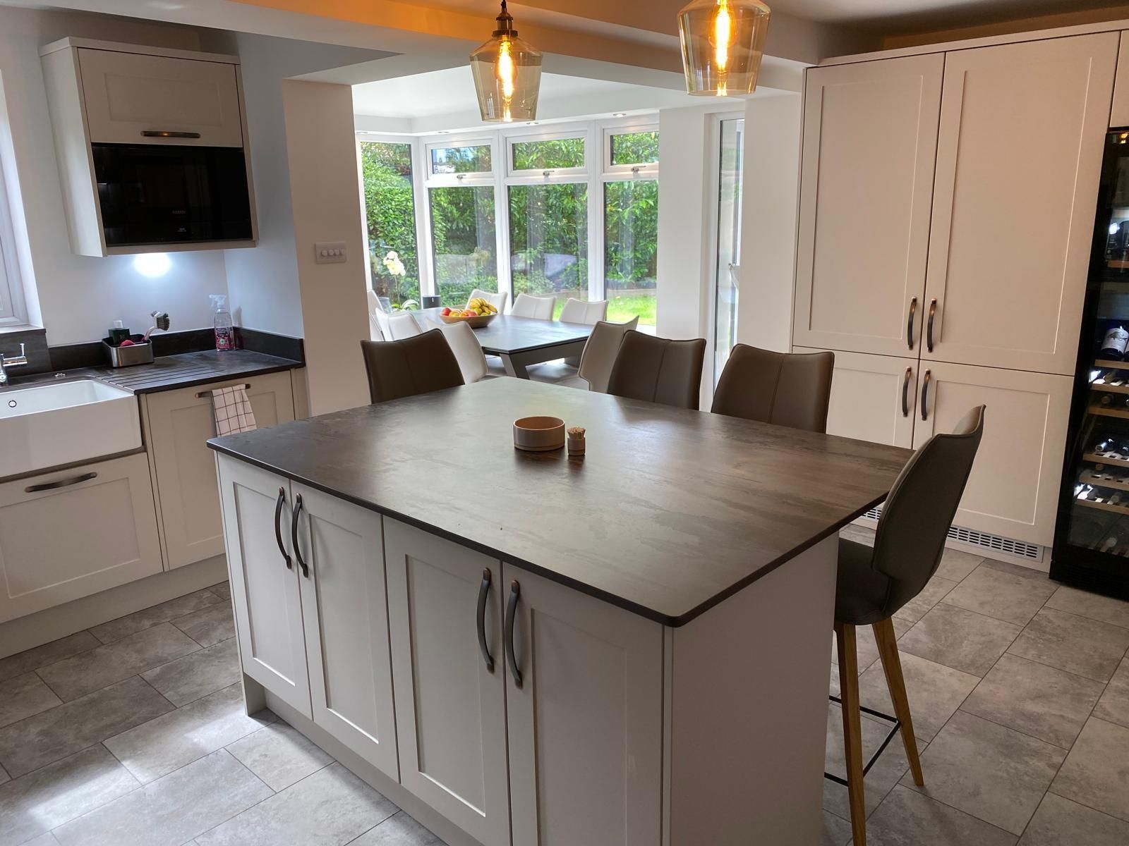 A modern kitchen with a large gray island, stools, and white cabinetry, opening into a bright conservatory dining area.