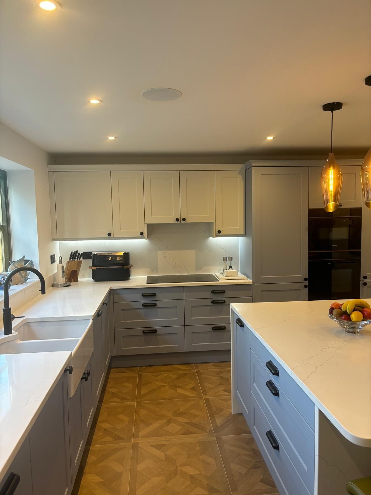 A modern kitchen featuring white upper cabinets, light gray lower cabinets, a white island, and patterned wood flooring.
