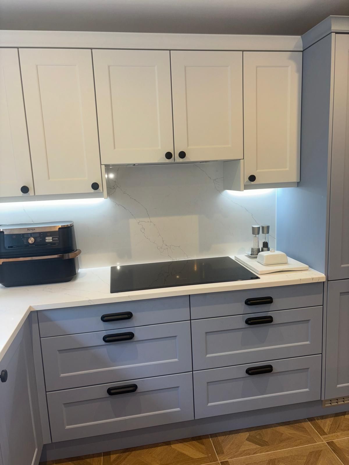 A modern kitchen featuring white cabinets, a black induction cooktop, a dark countertop, and light blue drawers.
