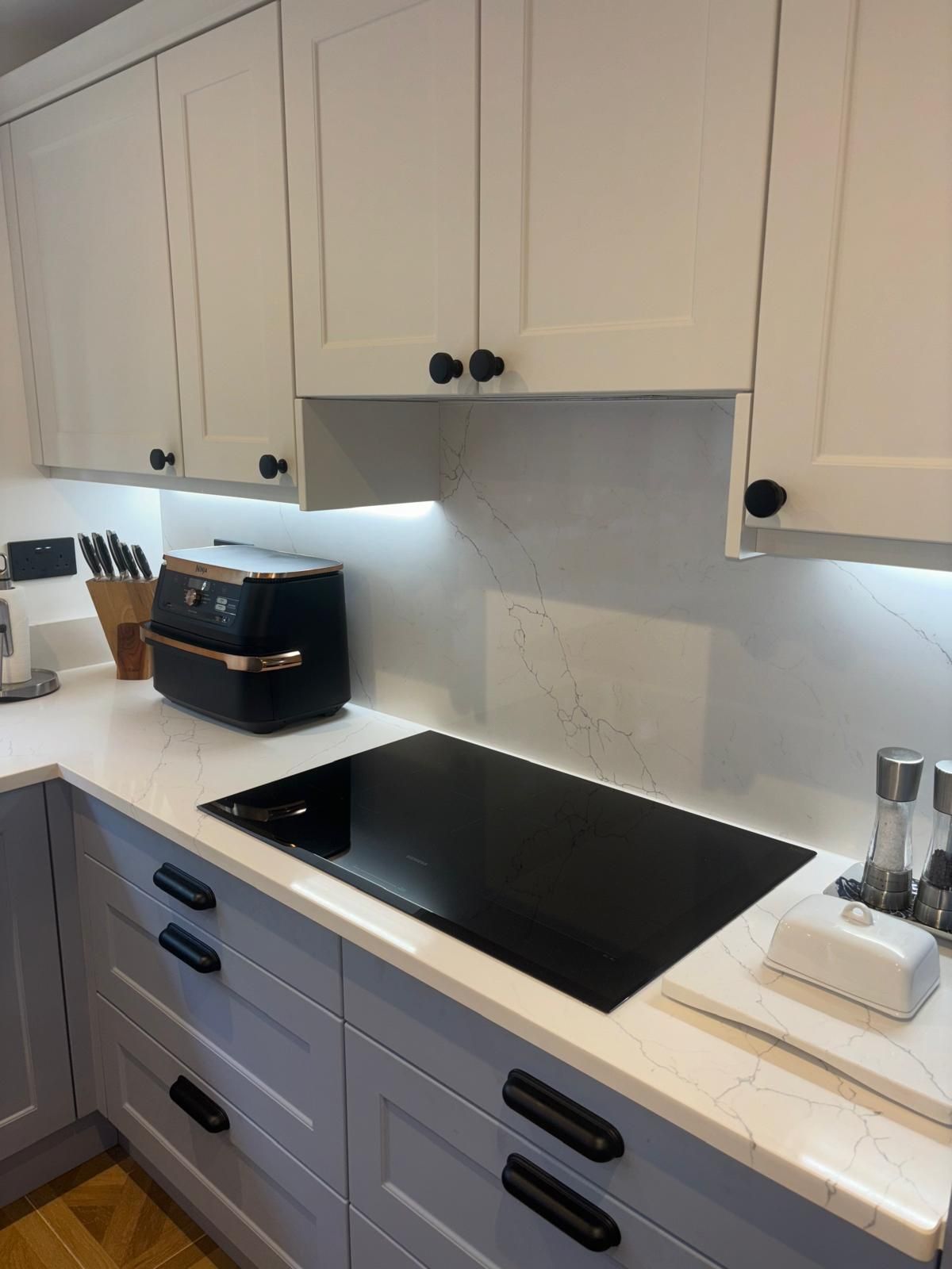 A kitchen counter featuring a black induction hob, a small black air fryer, and white cabinets with dark hardware.