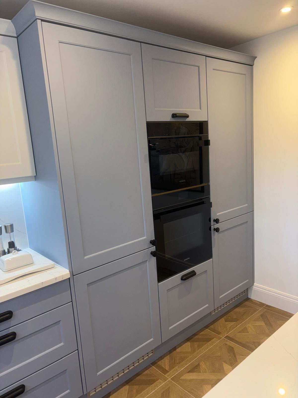 A kitchen wall unit with light blue shaker-style cabinets, featuring a built-in oven and microwave stack.