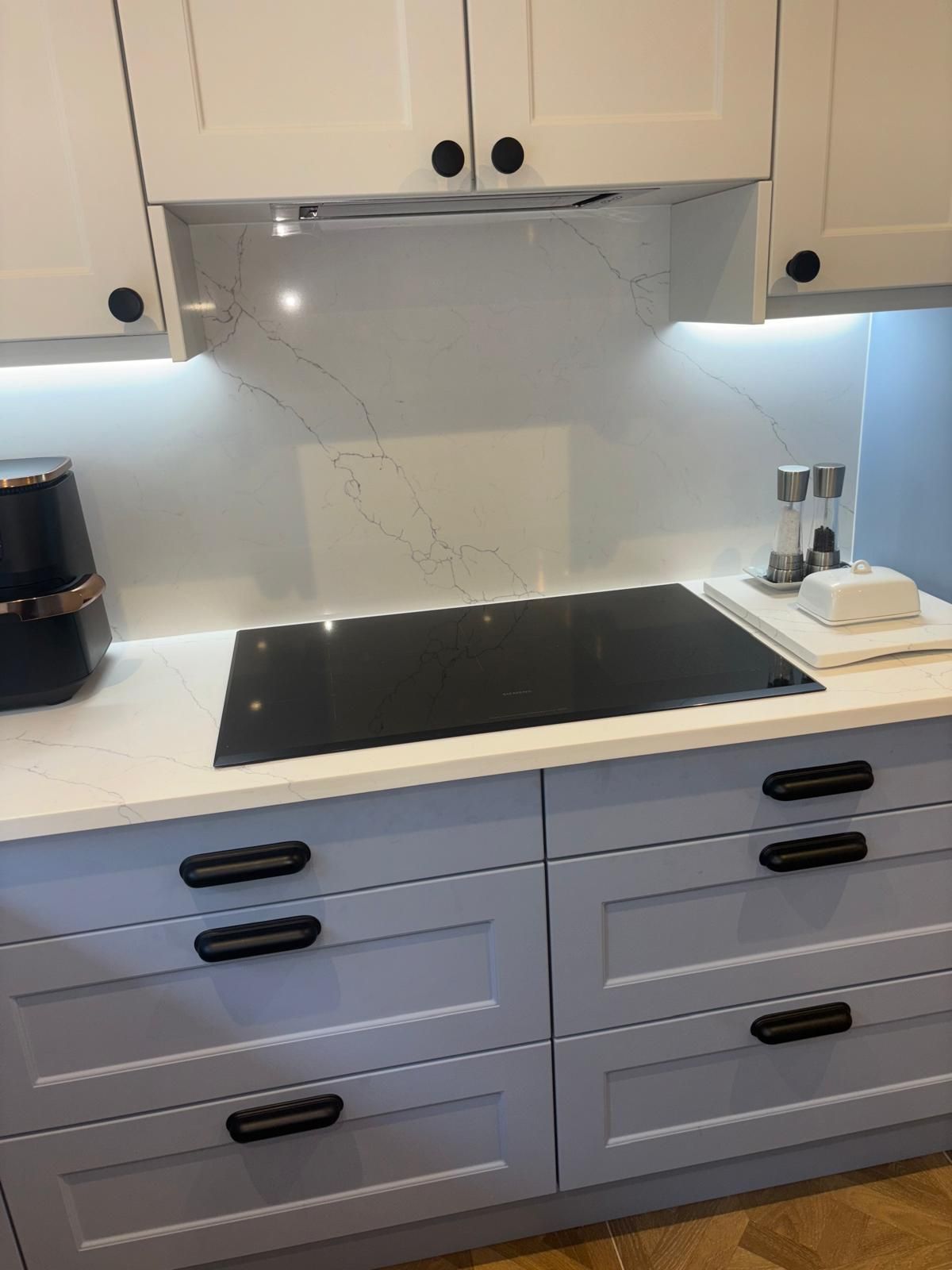 A kitchen stovetop with a marble-patterned backsplash, white countertops, and light blue cabinets with black handles.