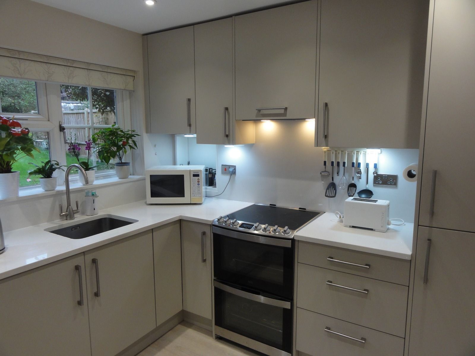 Modern kitchen with light grey cabinets, white countertops, stainless steel appliances, and a window over the sink.
