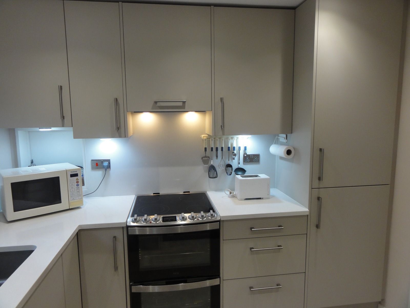A modern kitchen with light grey cabinets, a white countertop, an electric stove, a microwave, and a toaster.