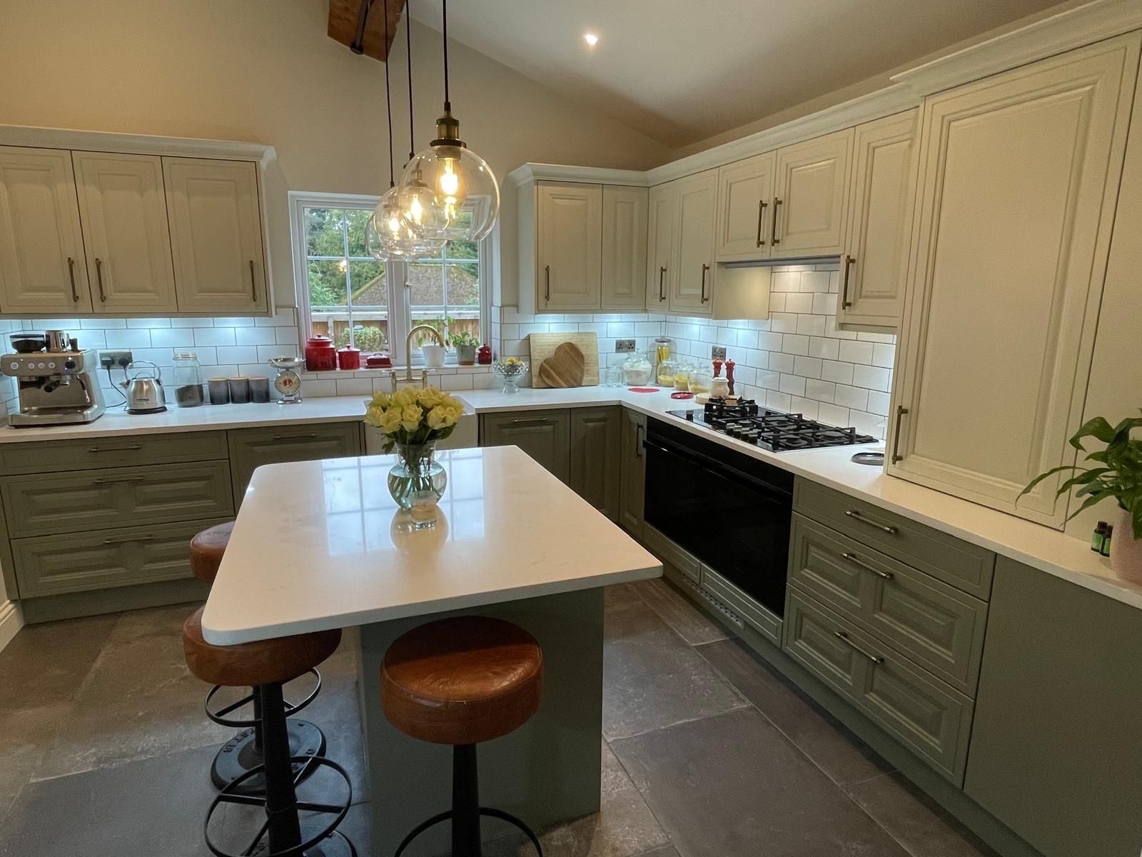 Modern kitchen featuring light green cabinets, a white marble island with two bar stools, and warm pendant lighting.