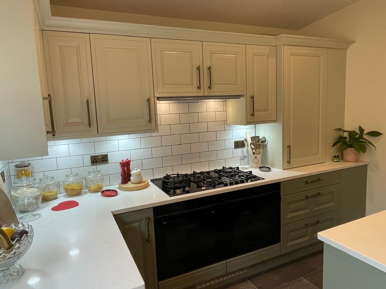 A modern kitchen with cream-colored upper cabinets, sage green lower cabinets, white countertops, and a tiled backsplash.