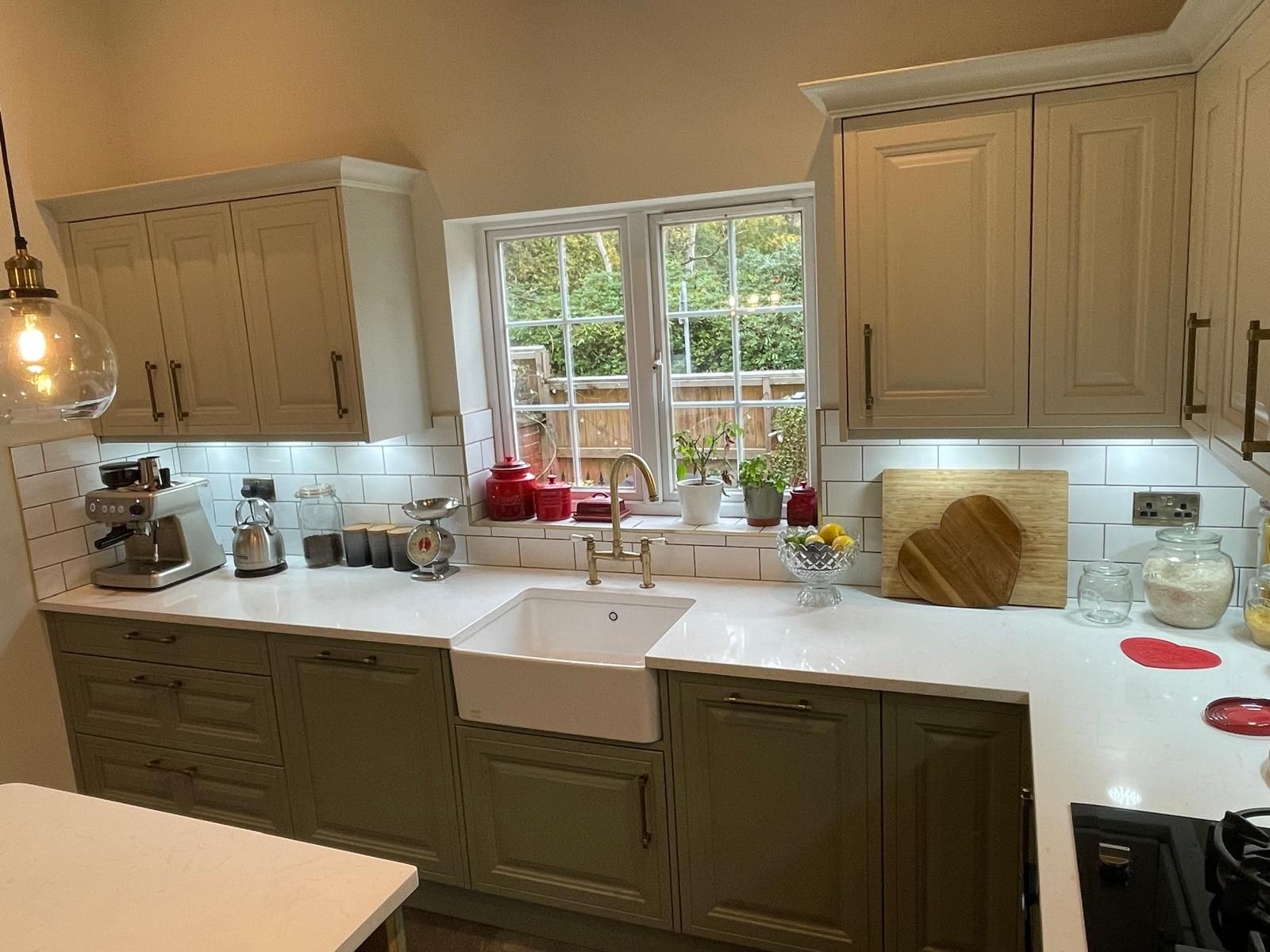 A bright kitchen with sage green lower cabinets, cream upper cabinets, a white farmhouse sink, and a view of trees.