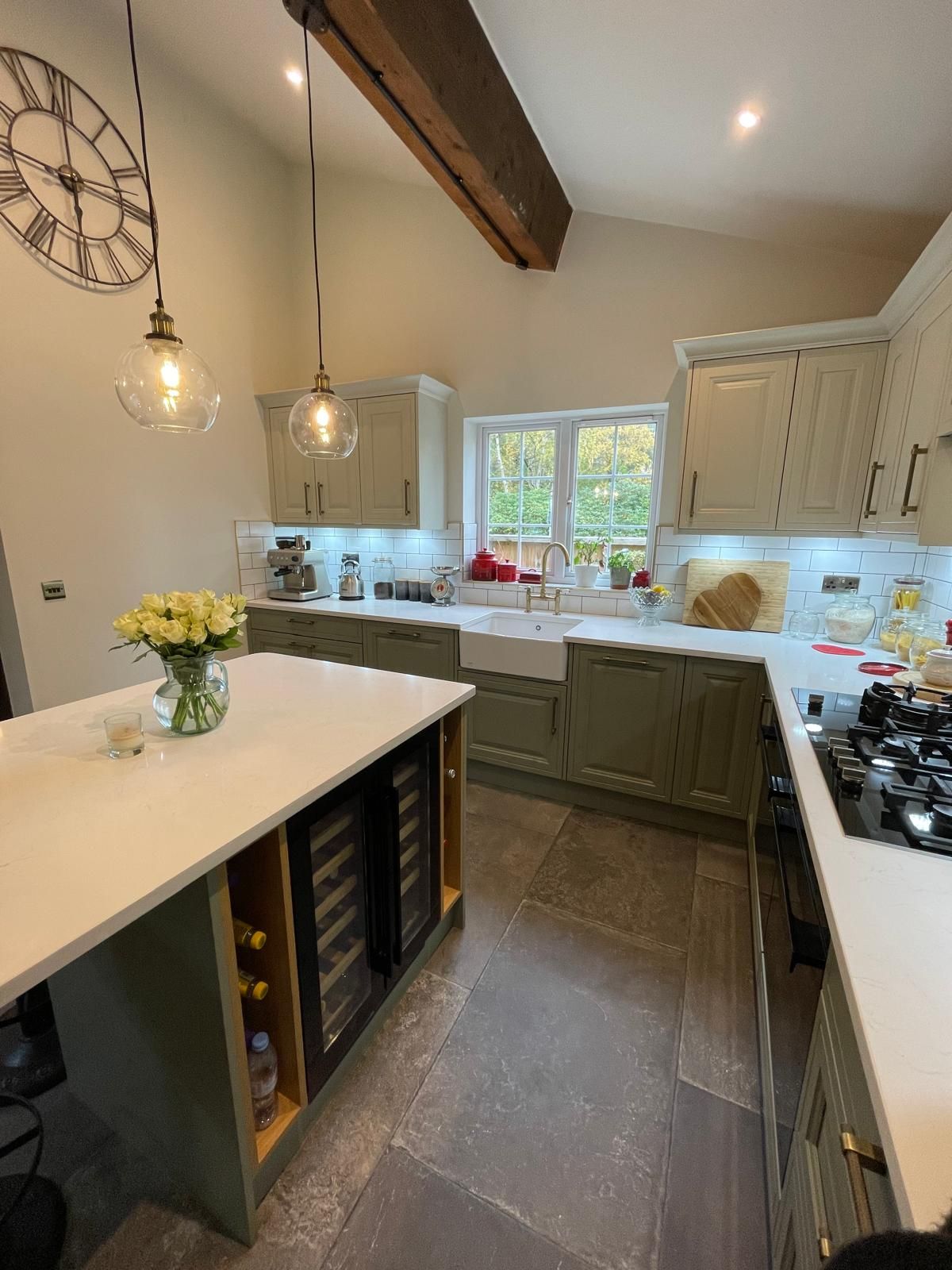 Modern kitchen featuring green cabinets, a central island with wine storage, white countertops, and a farmhouse sink.