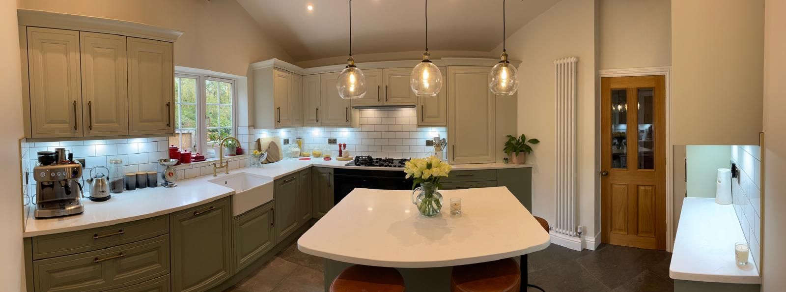 A modern kitchen with sage green cabinets, white countertops, a central island, and warm pendant lighting.