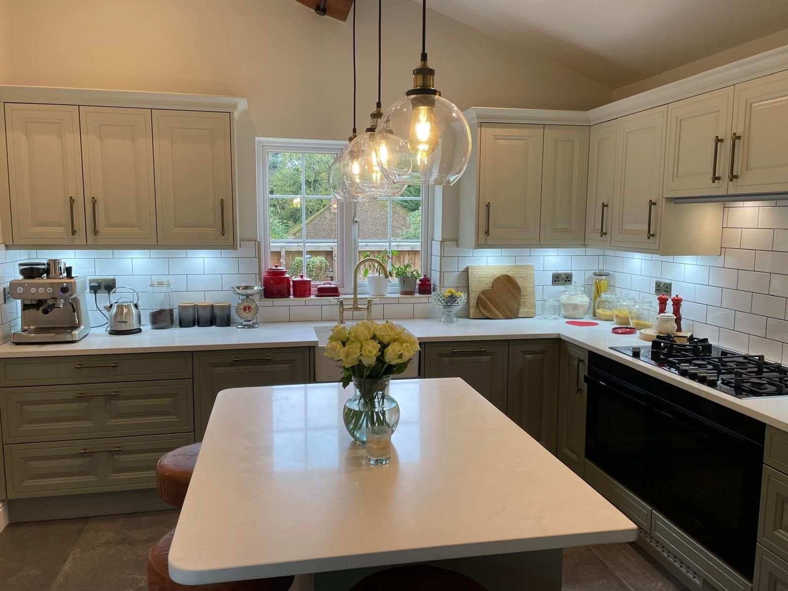 A light-colored kitchen featuring a central island with flowers, white countertops, gray lower cabinets, and pendant lights.