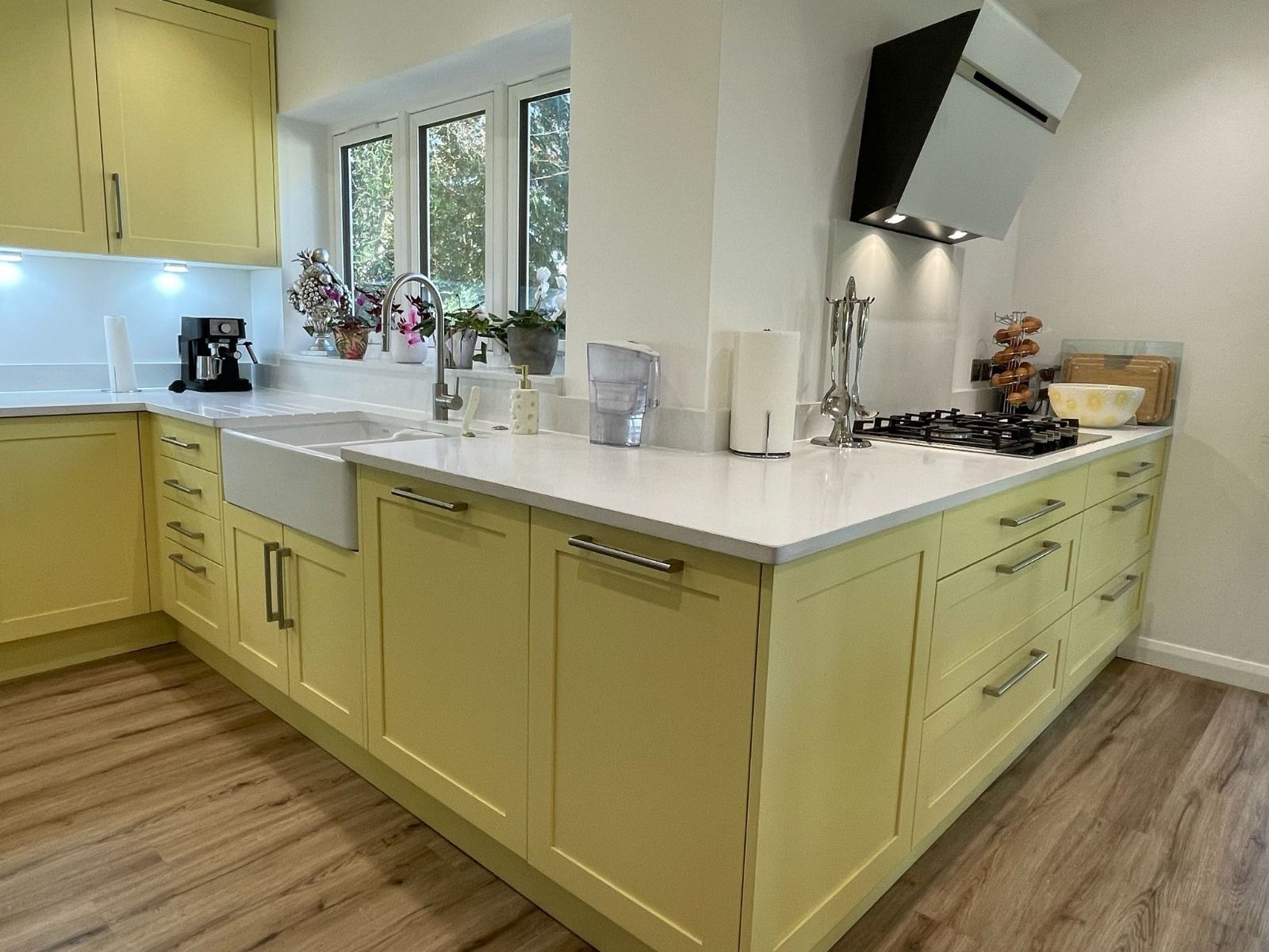 A sunny yellow kitchen with white countertops, a farmhouse sink, and wood-patterned flooring.