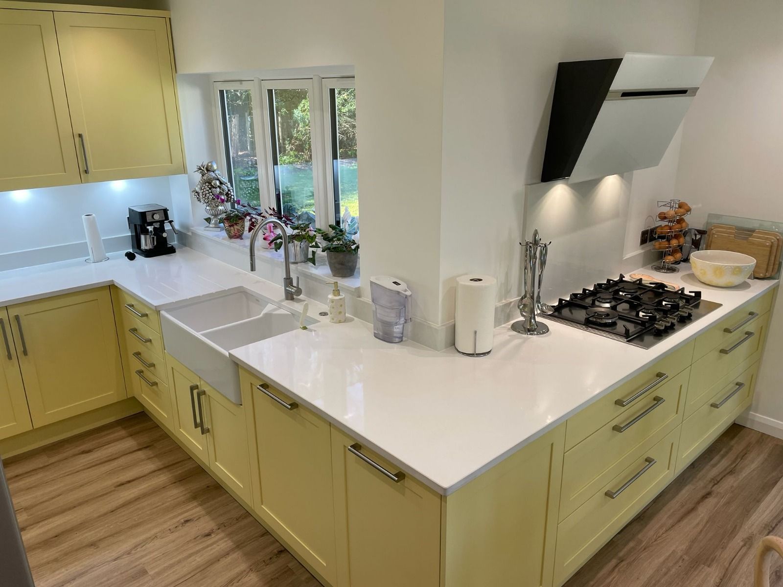 A kitchen with yellow cabinets, white countertops, a double basin sink, a gas stovetop, and an angled range hood.