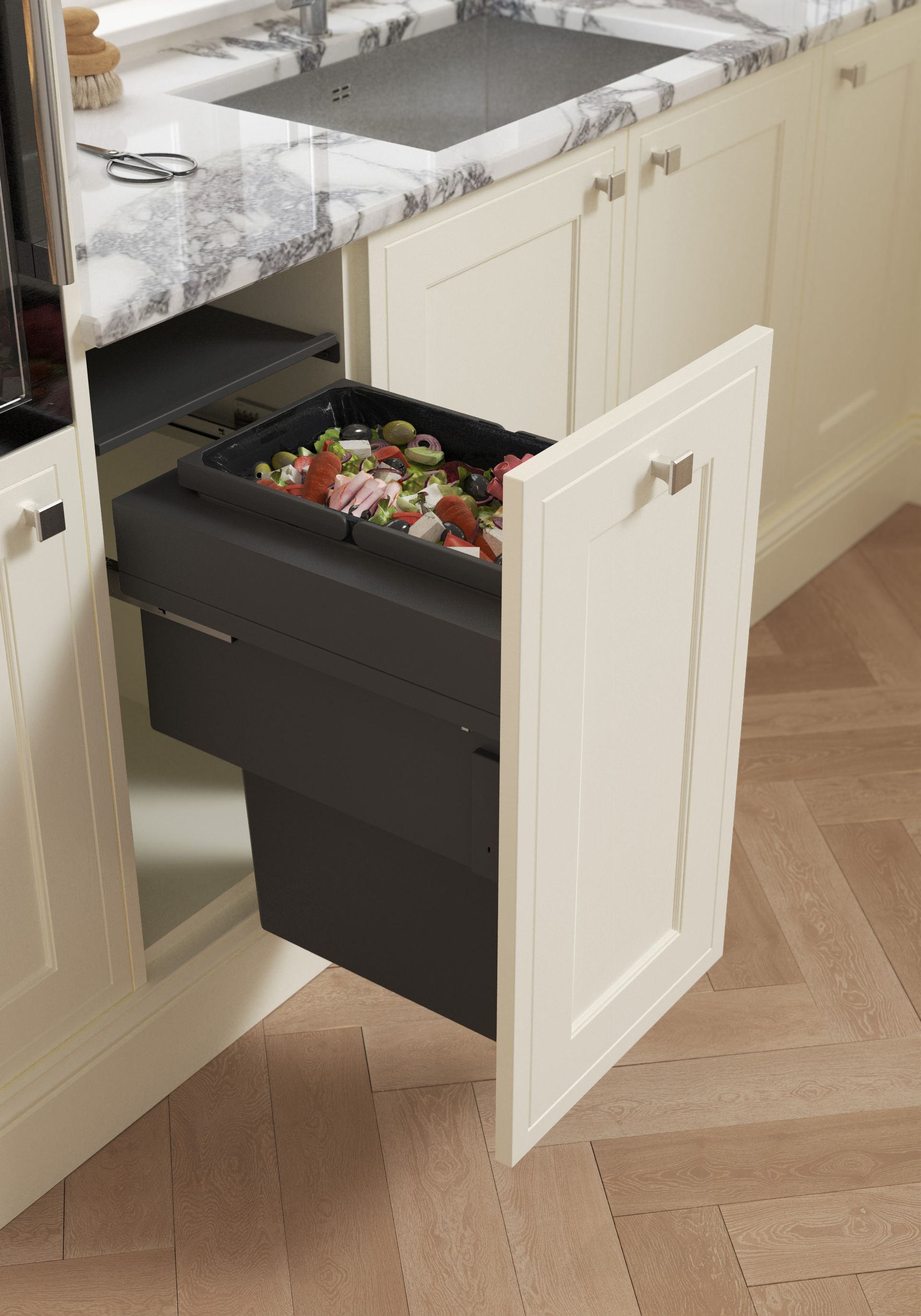 A pull-out kitchen cabinet drawer with a black bin filled with food scraps, positioned under a marble-patterned counter.