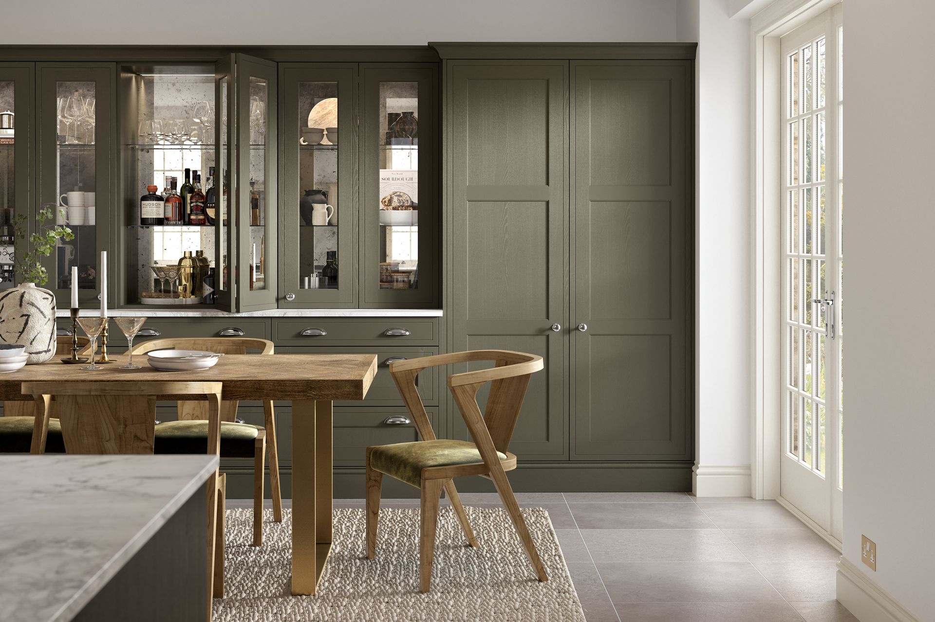 A dining area with a rustic wooden table, two chairs, and sage green shaker-style cabinets with glass display doors.
