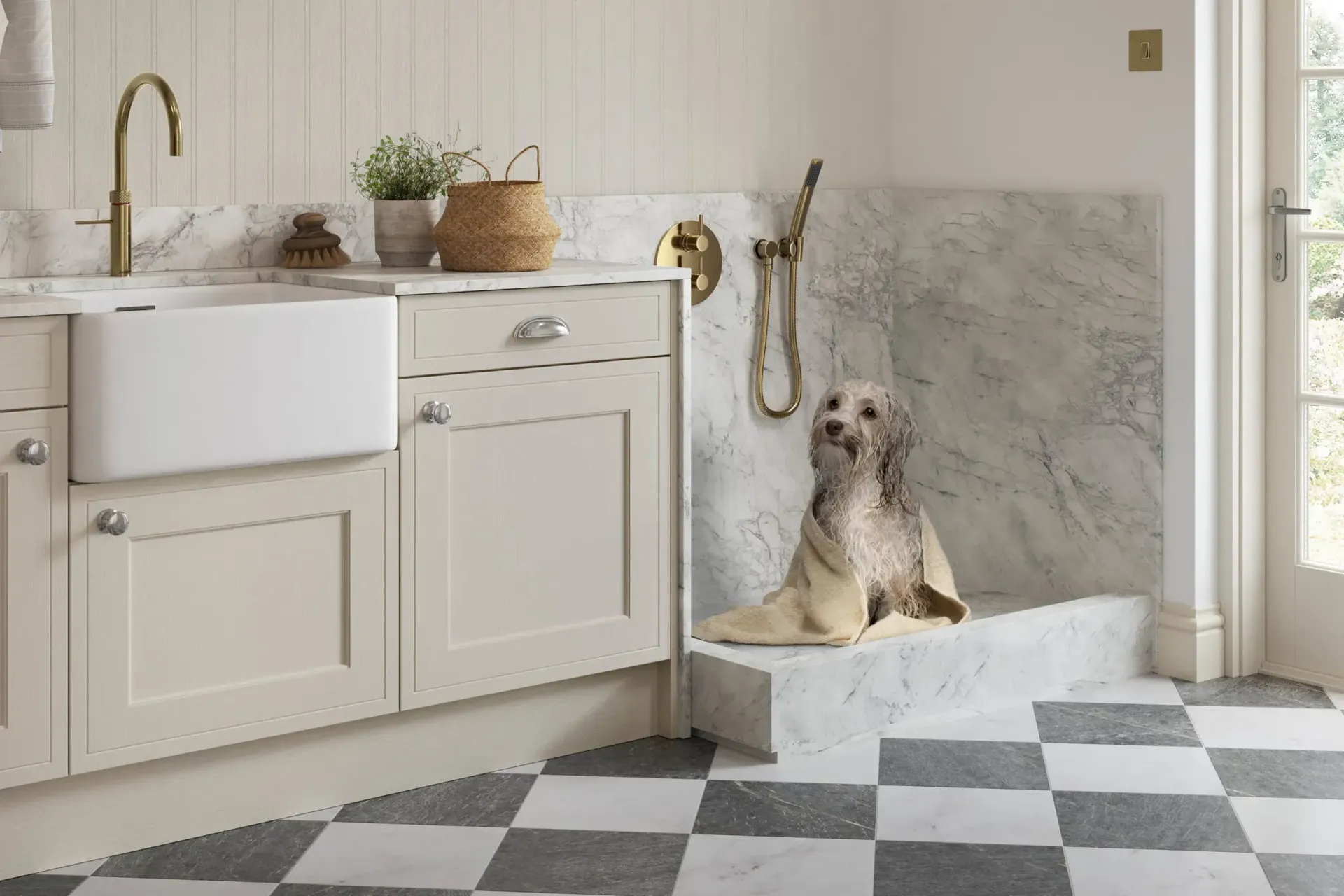 A shaggy dog sits in a marble-tiled dog wash station next to a farmhouse sink in a kitchen with black and white tile floors.