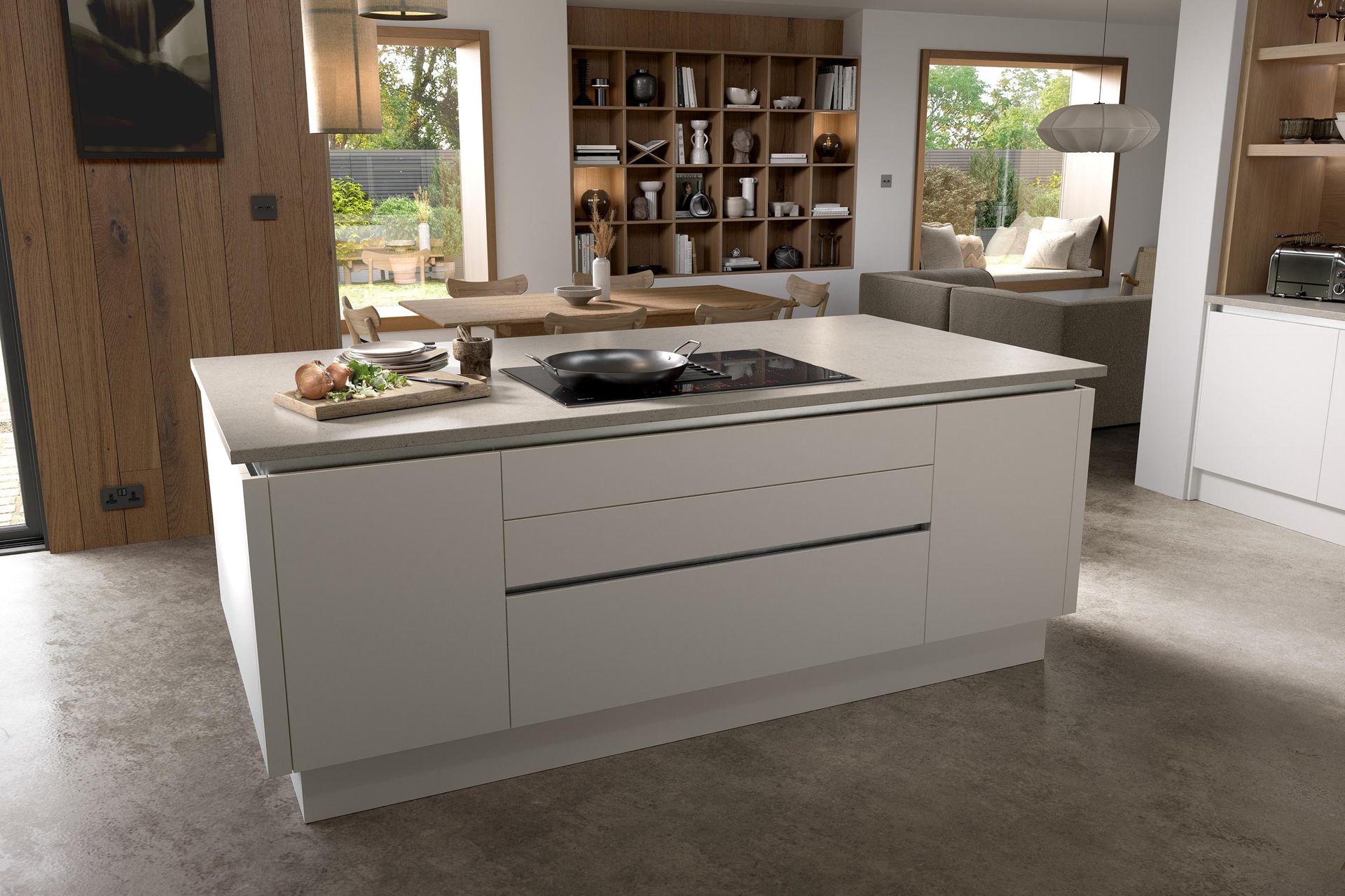 A modern white kitchen island with a built-in cooktop and cutting board sits in a bright, open-plan home interior.