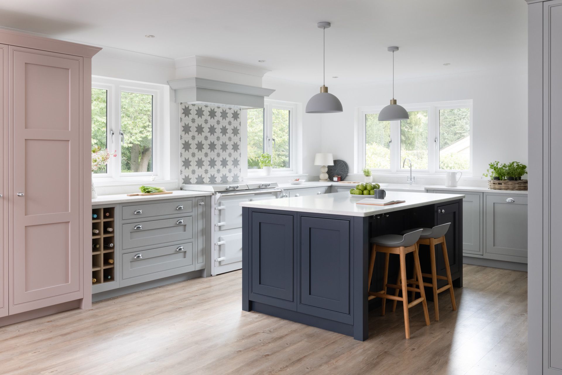 Spacious kitchen with a light pink cabinet, dark blue kitchen island with stools, gray cupboards, and white countertops.