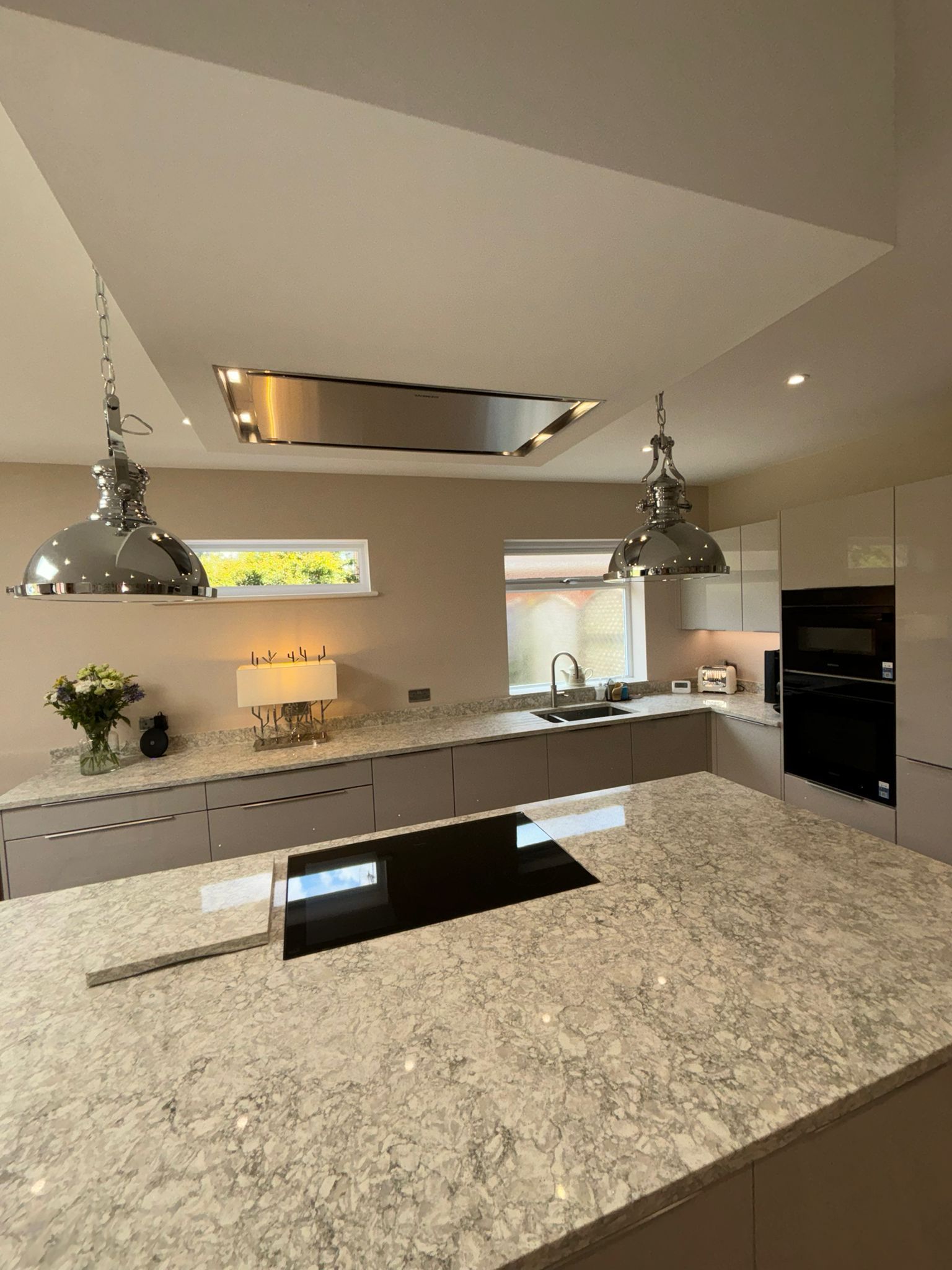 Modern kitchen with a granite island, a built-in cooktop, two hanging pendant lights, and light-colored cabinetry.