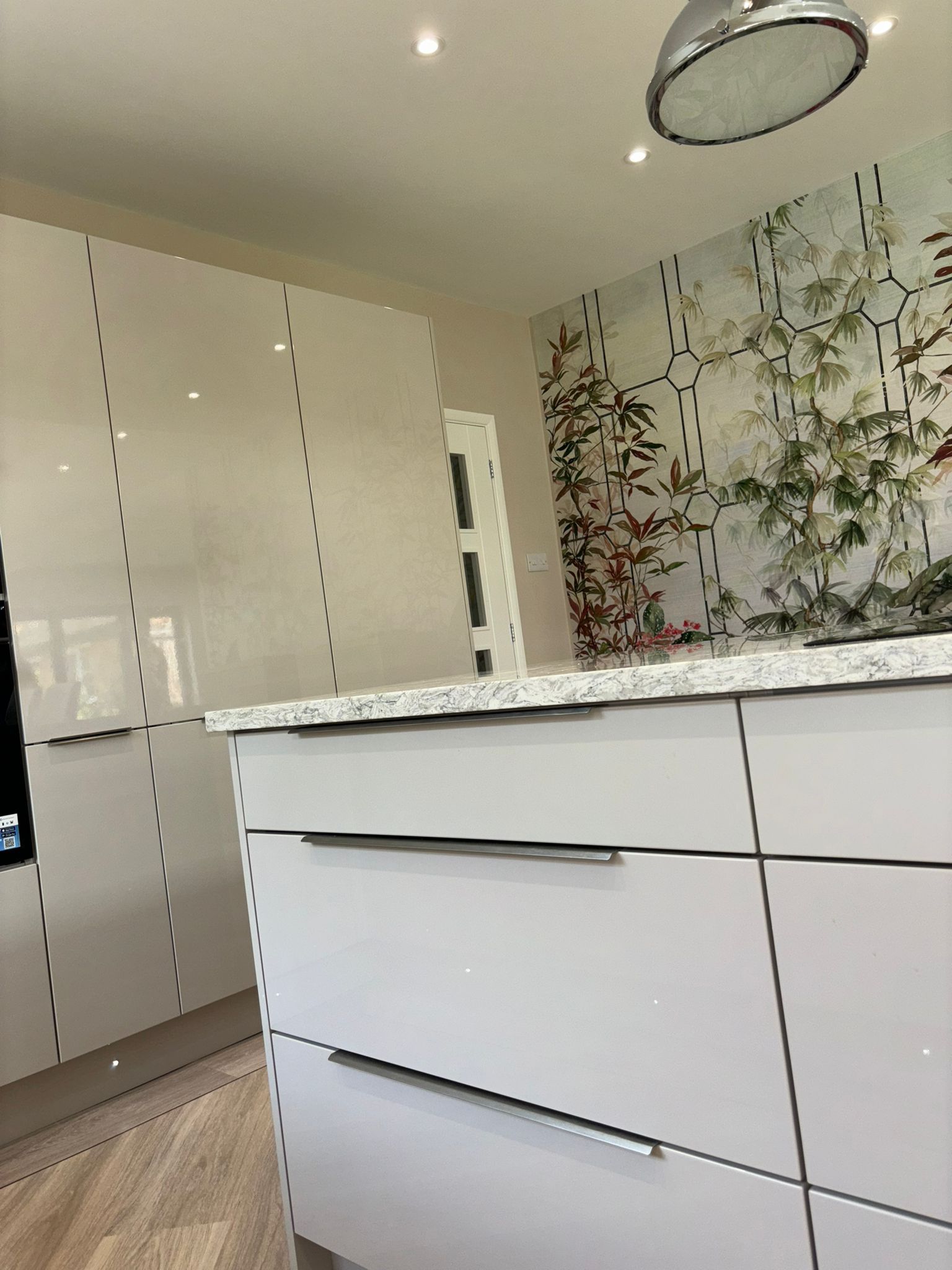 A kitchen island with white drawers and a granite-style countertop, set against a wall featuring botanical wallpaper.