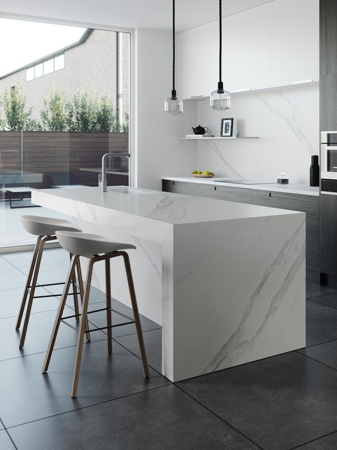 Modern kitchen with a white marble waterfall island, two bar stools, and dark tiled flooring looking out to a patio.