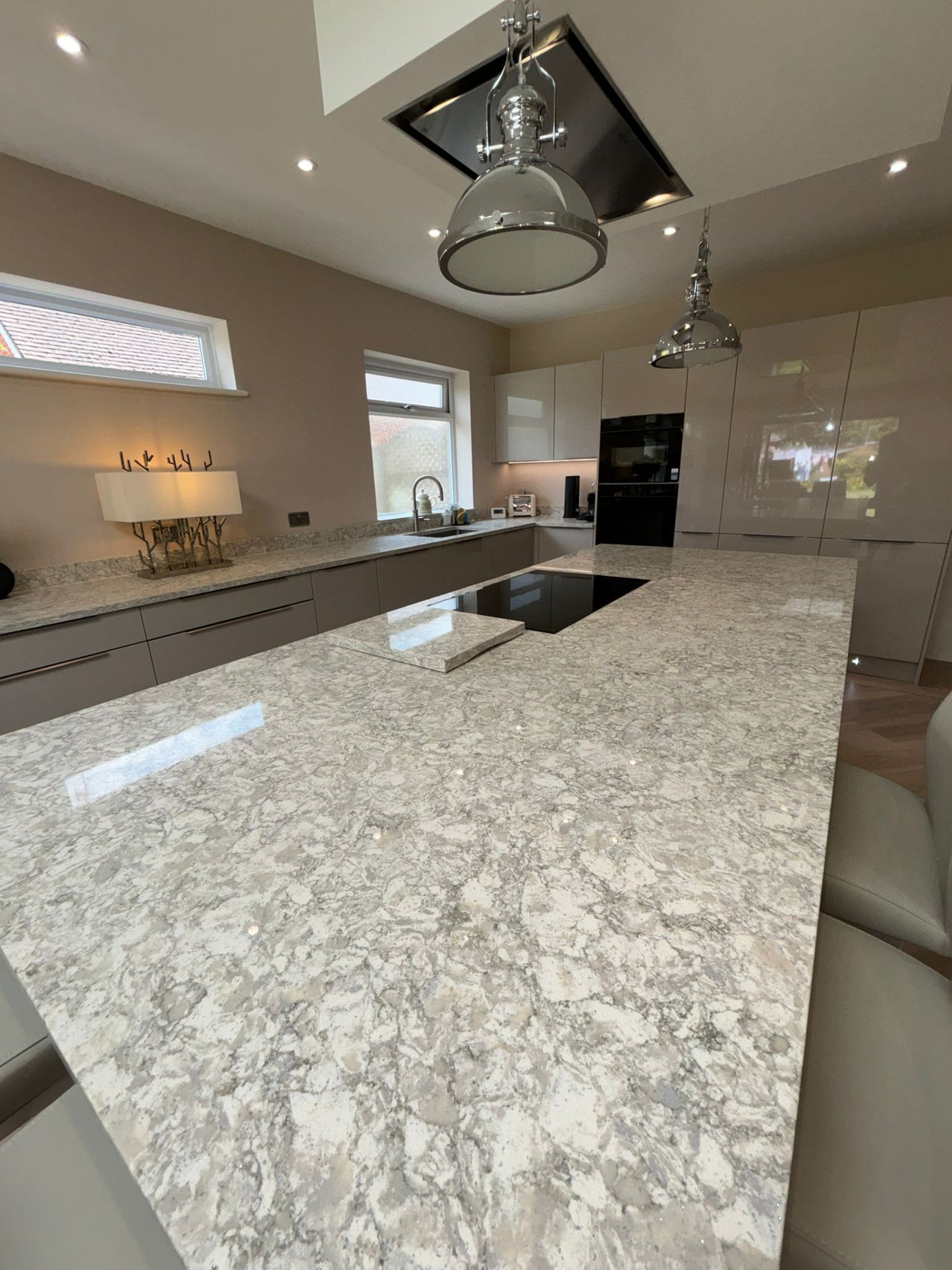 A modern kitchen island with a white and gray marbled countertop, featuring a stovetop and pendant lights overhead.