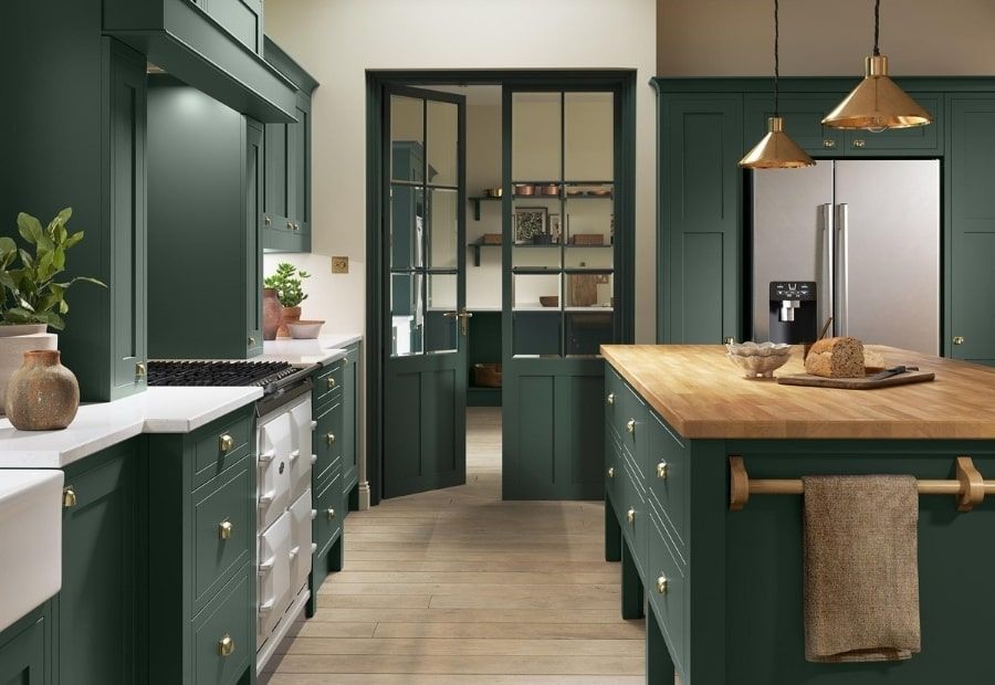 A stylish kitchen featuring dark green cabinetry, a wooden island countertop, brass hardware, and a glass-paned double door.