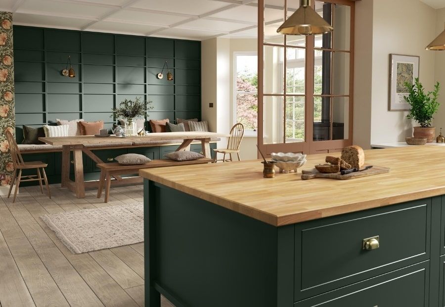 A kitchen interior with a dark green island, wooden countertop, dining table, and built-in bench against a paneled wall.