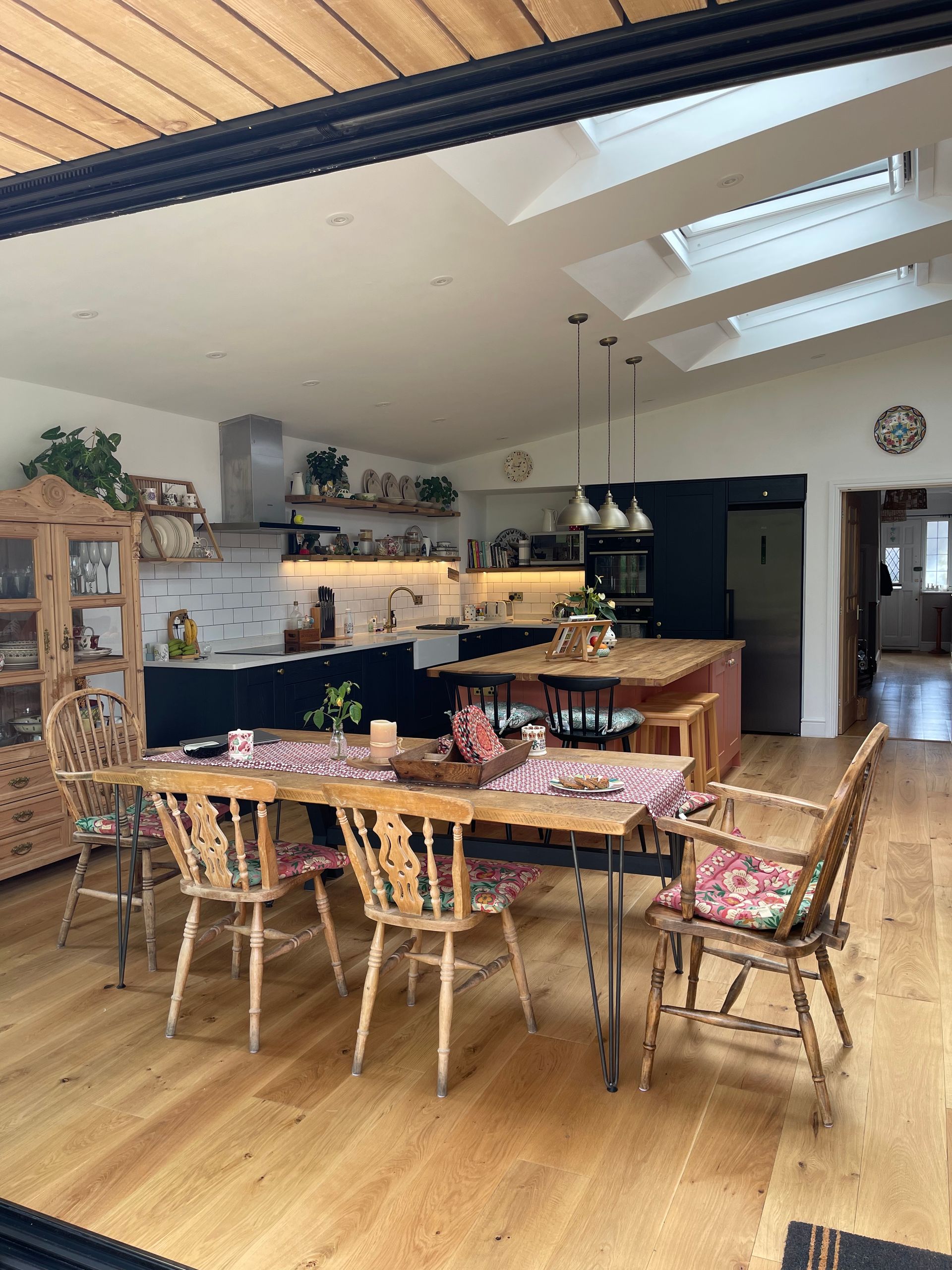 A spacious, bright kitchen and dining area featuring a wooden table with floral chairs, pendant lights, and skylights.