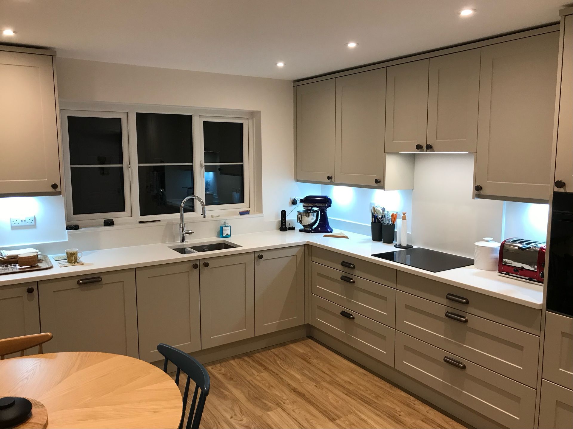 A modern kitchen with light grey cabinets, white countertops, stainless steel appliances, and wood-effect flooring.