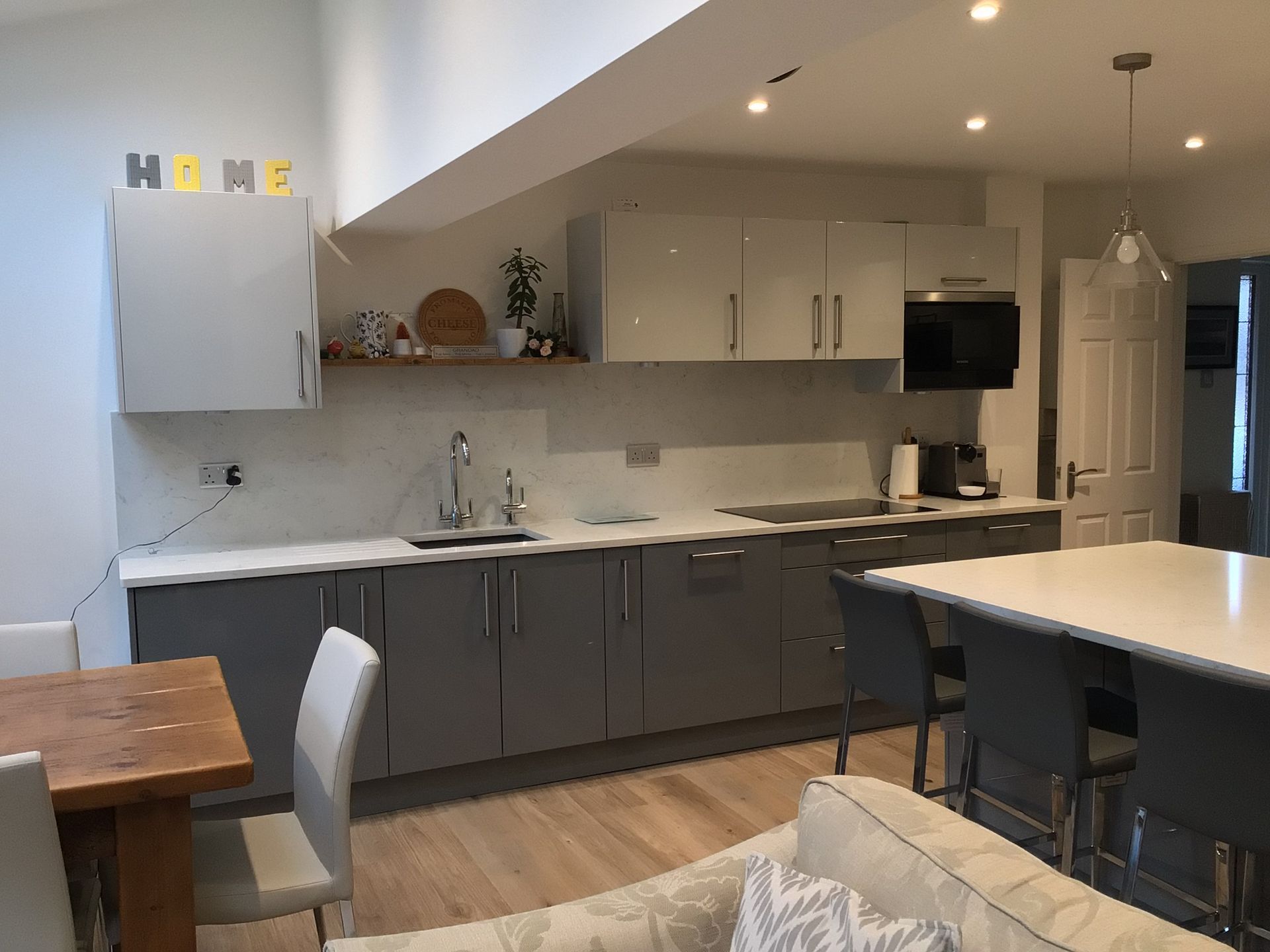 A modern kitchen featuring grey lower cabinets, white upper cabinets, a white countertop, and a dining area with stools.