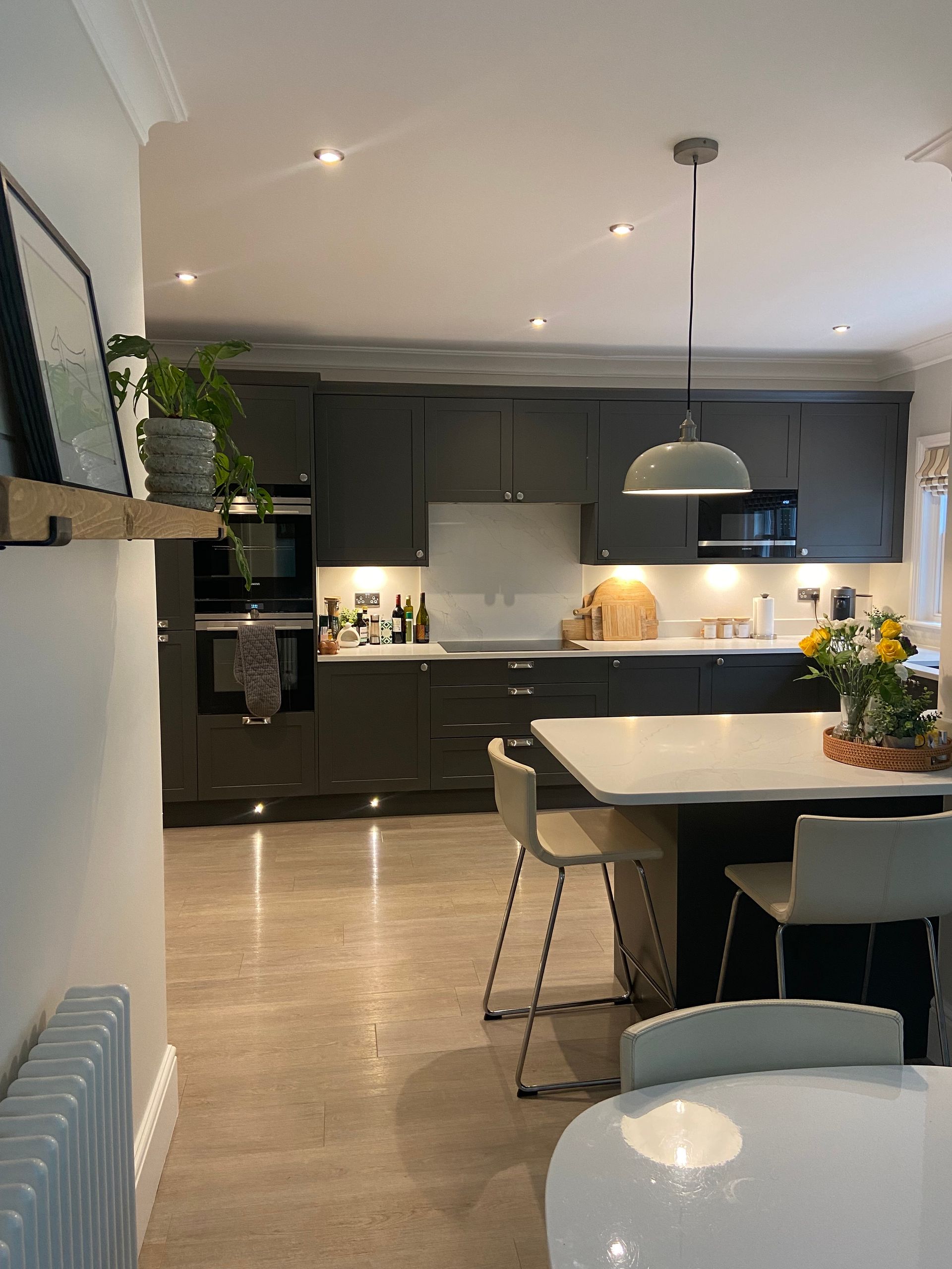 A modern kitchen with dark gray cabinets, a white island, tiled floor, and a hanging pendant light over the counter.