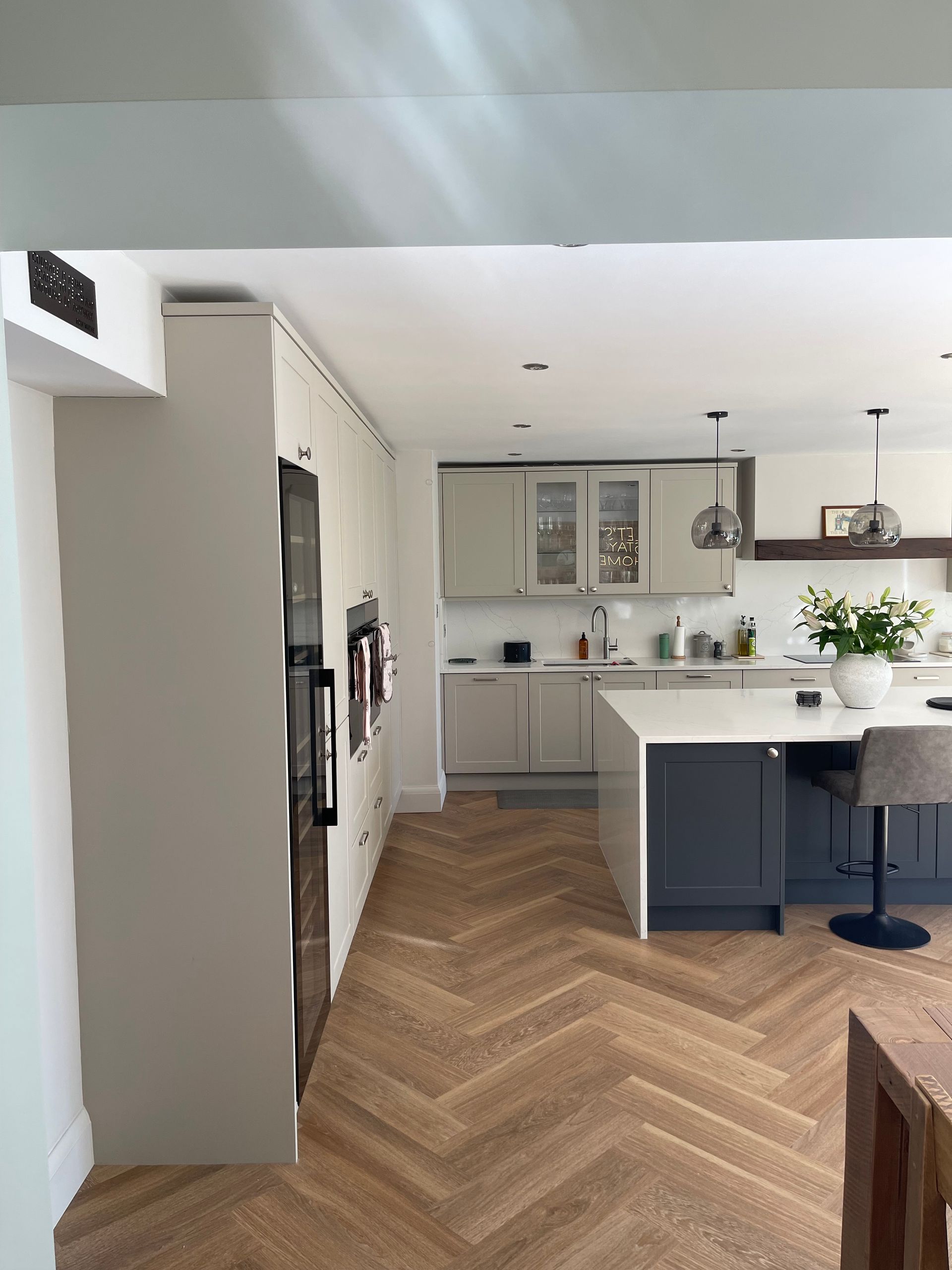 Modern kitchen with white and dark gray cabinetry, a central island with bar seating, and light-toned herringbone flooring.