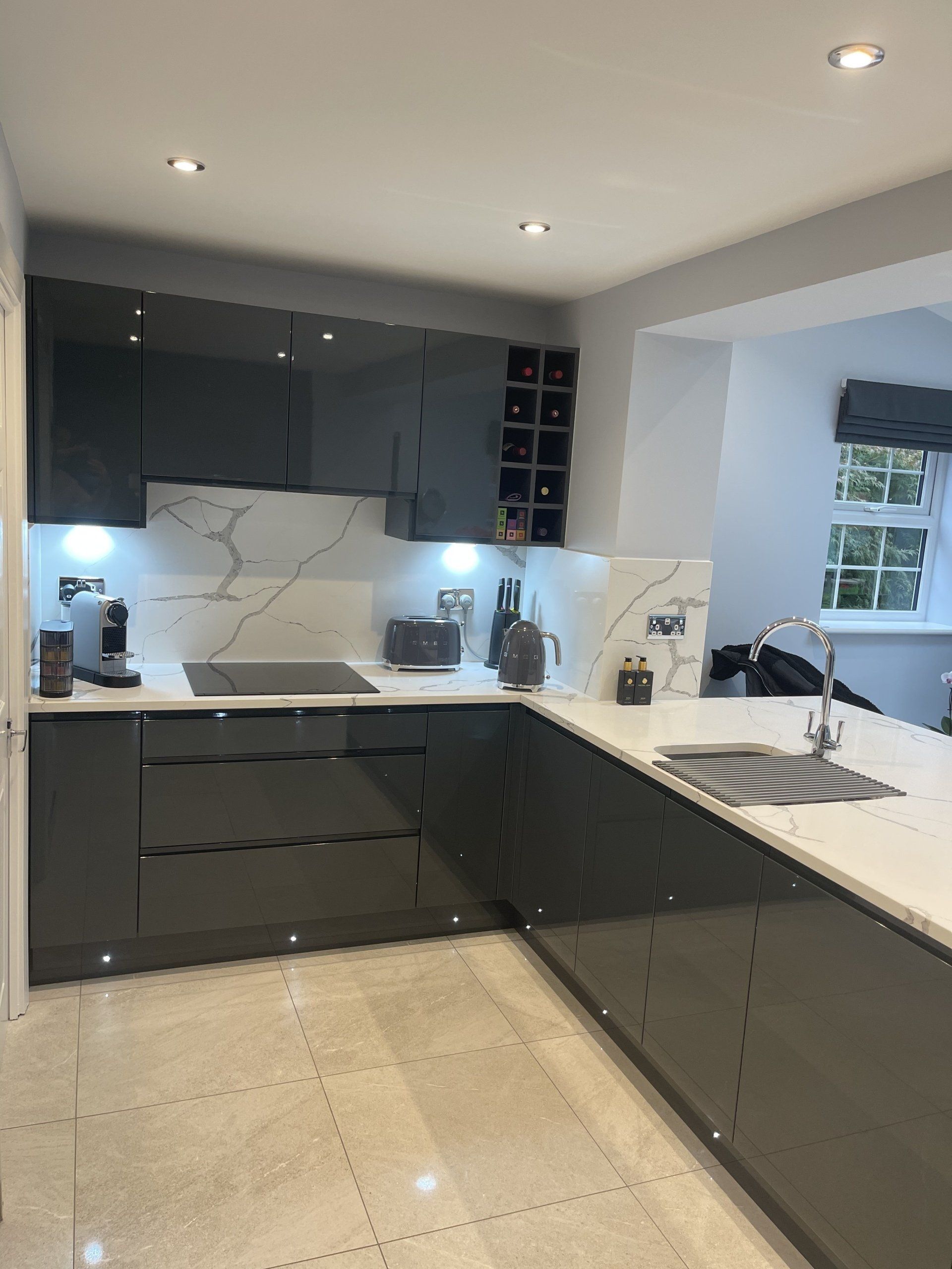 Modern kitchen with dark grey cabinets, white marble countertops, and tiled floors in a bright, open-plan space.