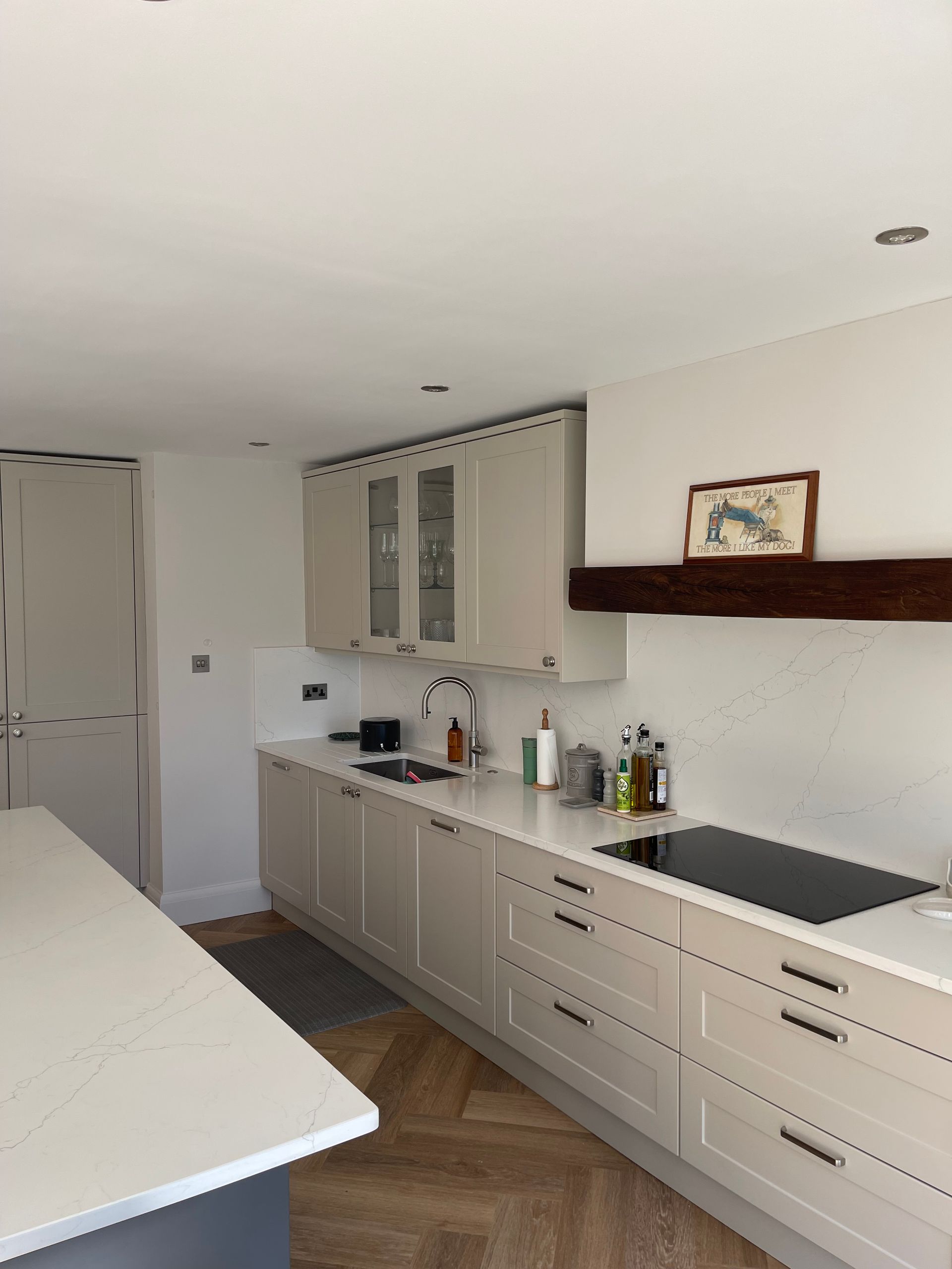 A modern kitchen featuring light beige cabinets, a white countertop, a wood-beam range hood, and herringbone wood floors.