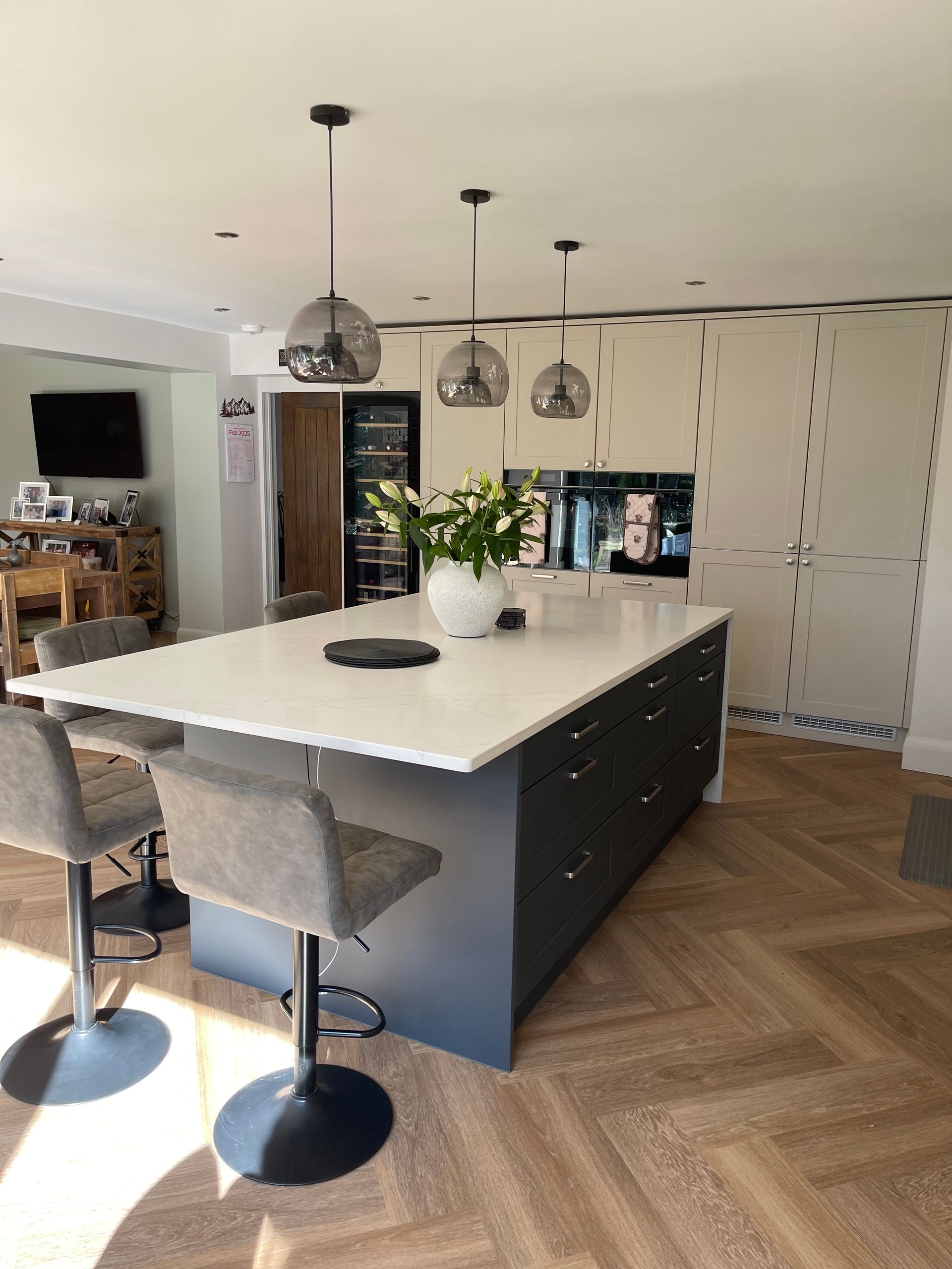 A modern kitchen with a large dark blue island, white countertop, three pendant lights, and light wood herringbone floors.