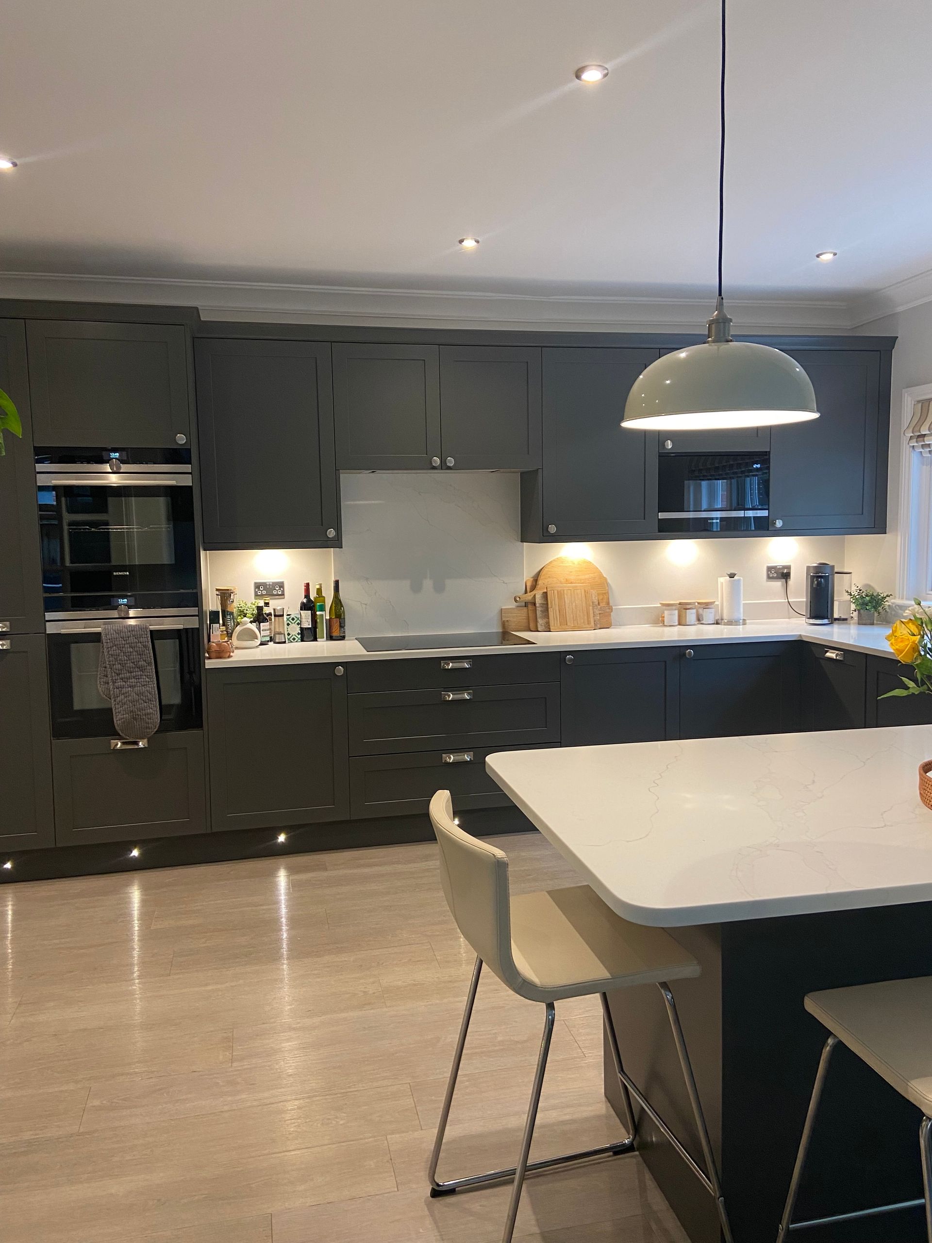 Modern kitchen with dark cabinetry, white countertops, an island with two stools, and a pendant light overhead.