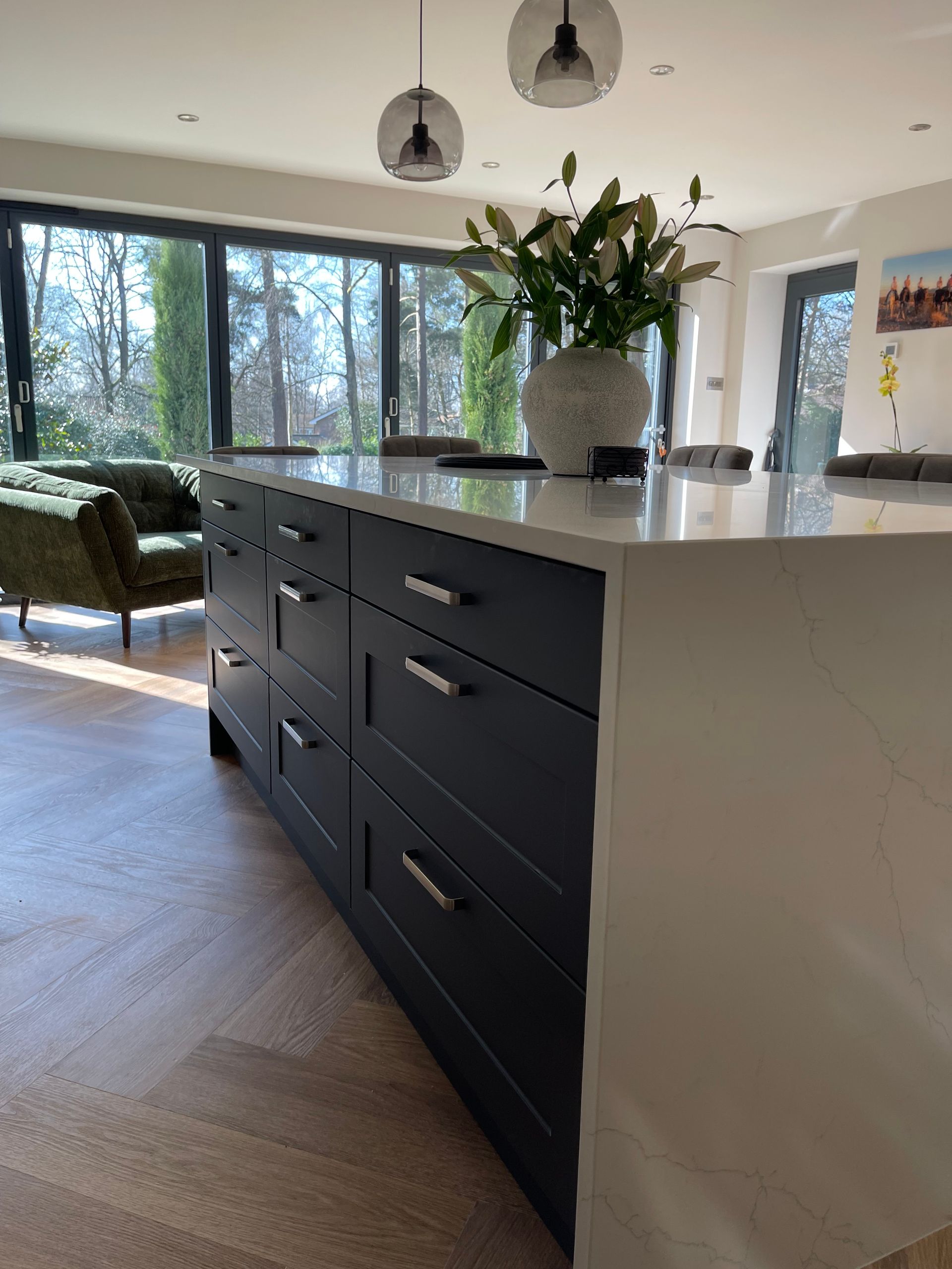 A dark navy kitchen island with white stone countertop and metal hardware, set in a room with wood flooring and patio doors.