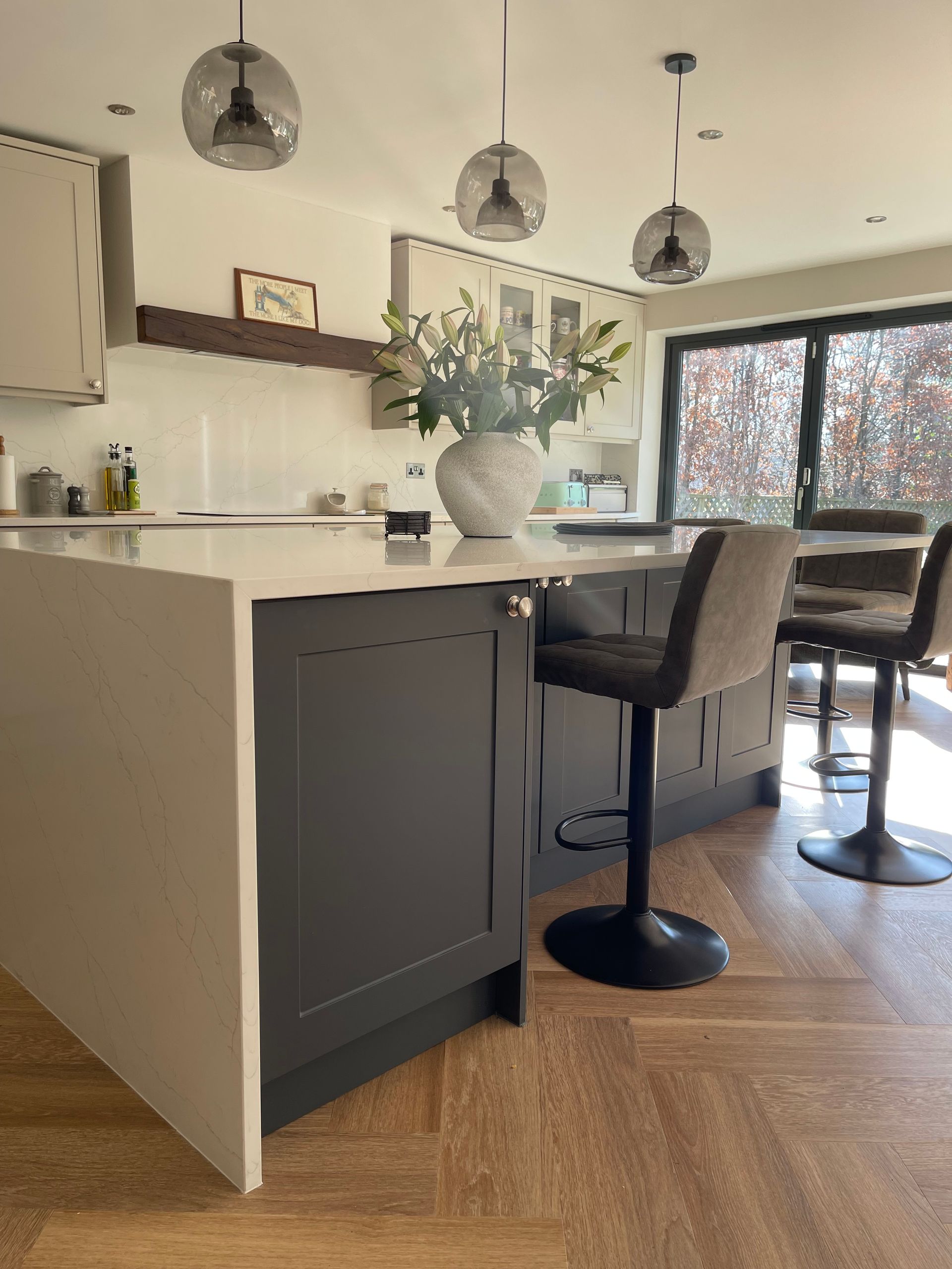 A kitchen island with dark gray cabinetry and a white countertop, featuring two bar stools and pendant lights overhead.