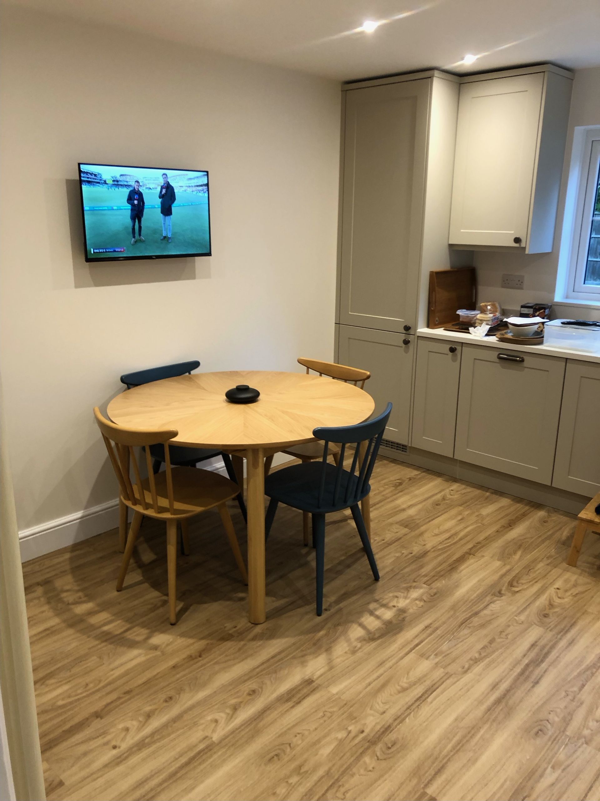 A small round wooden dining table with four mismatched chairs in a kitchen with light-colored cabinets and wood flooring.