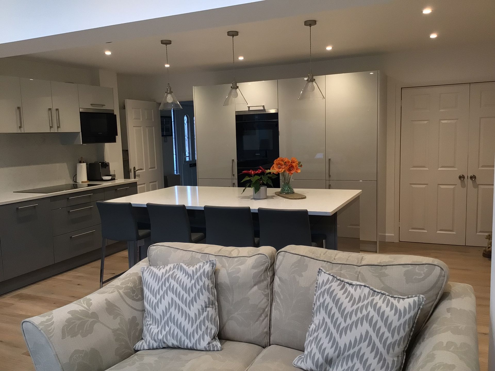 A modern kitchen with grey cabinetry, a large white island with seating, and a beige sofa in the foreground.