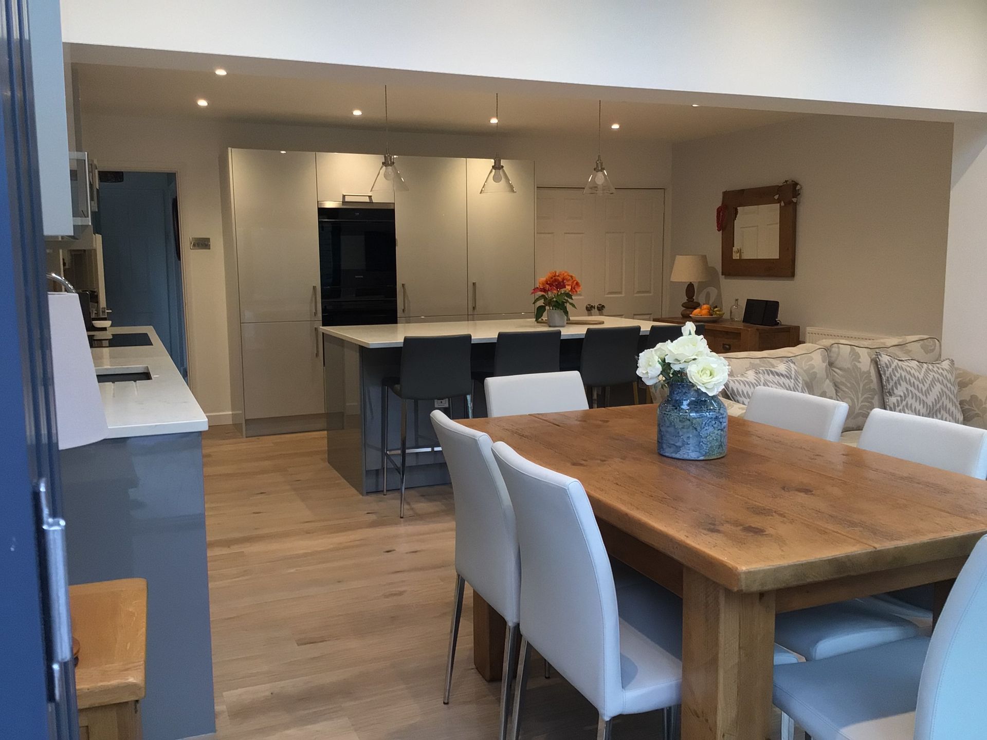 Open-plan kitchen and dining area with a wooden table, white chairs, a kitchen island, and light-colored cabinetry.